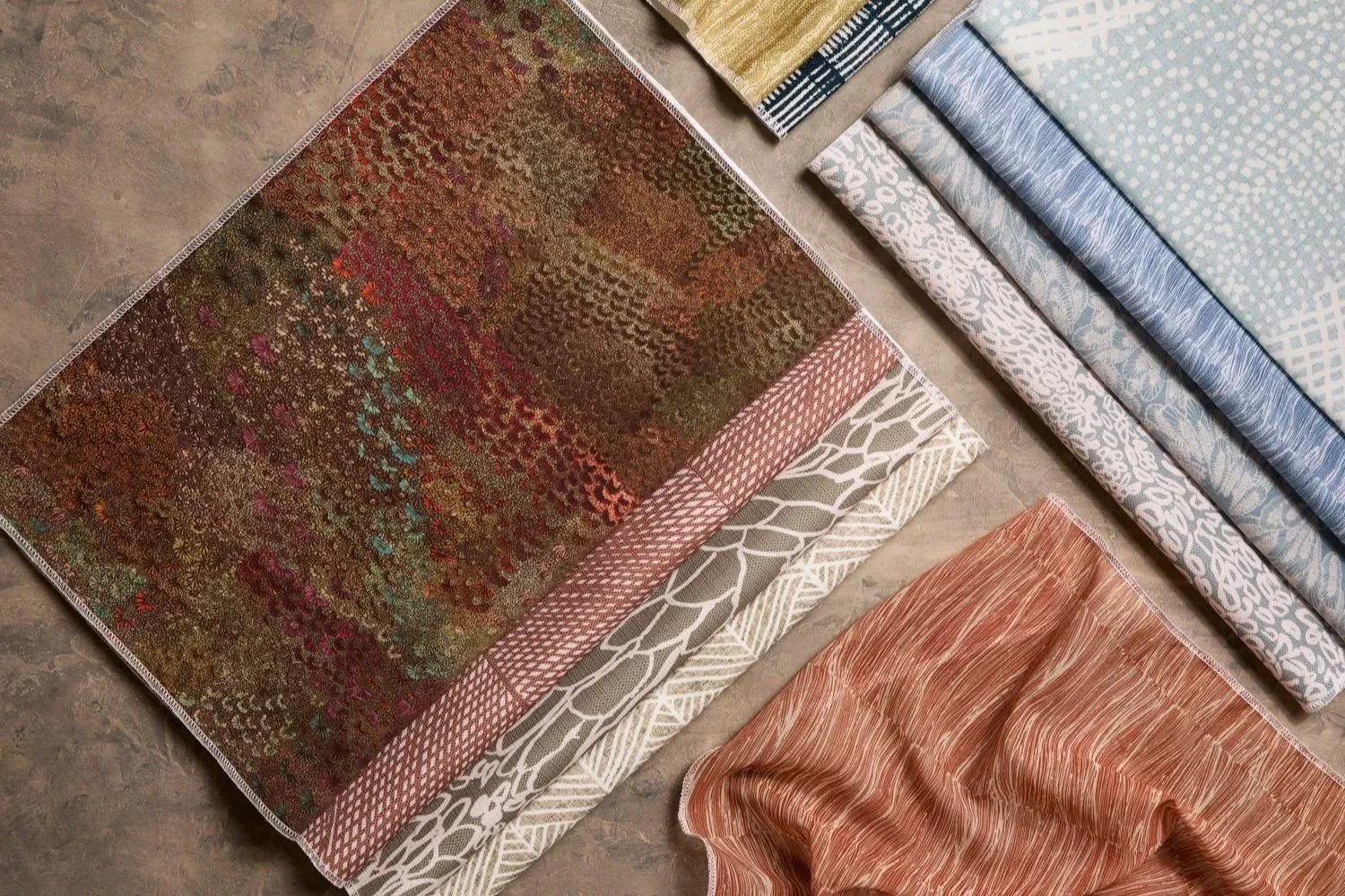 Large assortment of patterned fabric swatches arranged on a table, featuring various First Nations designs and colours including brown, plum, green, blue, beige, orange, white.