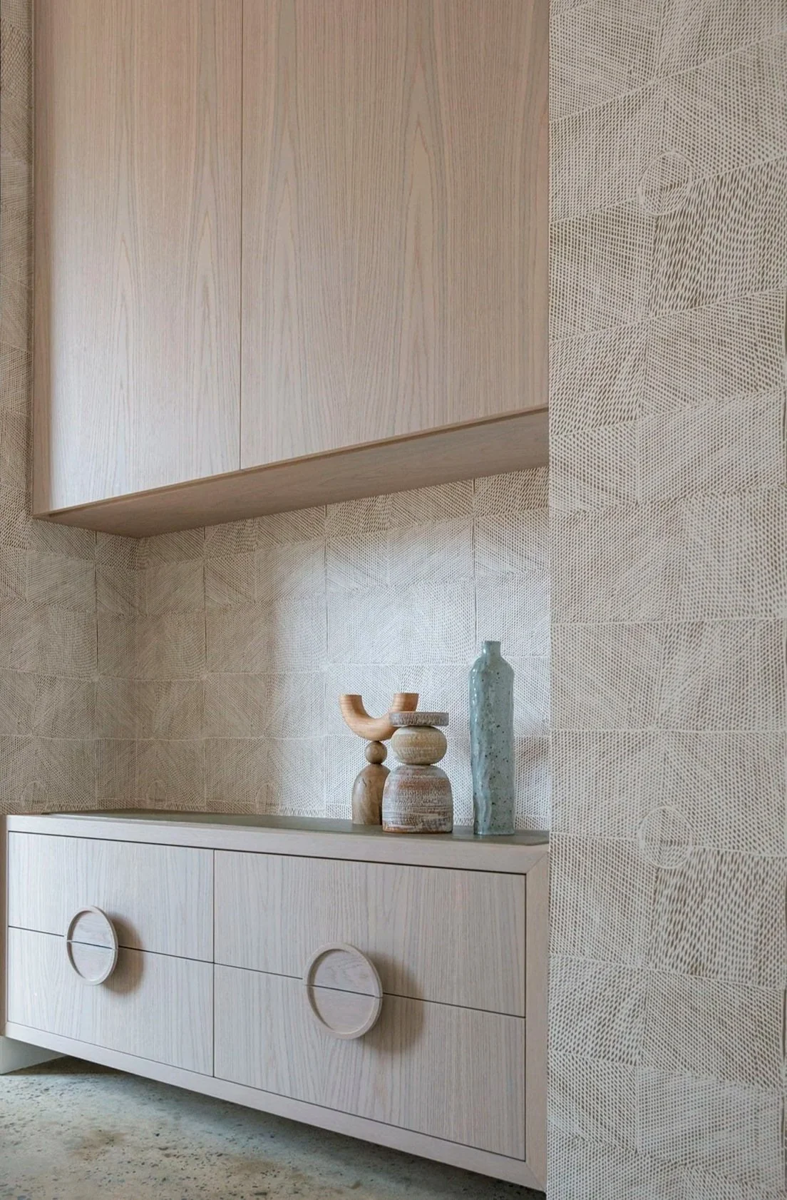 Minimalist wooden cabinet with decorative vases, set against a patterned textured wall in a modern interior.