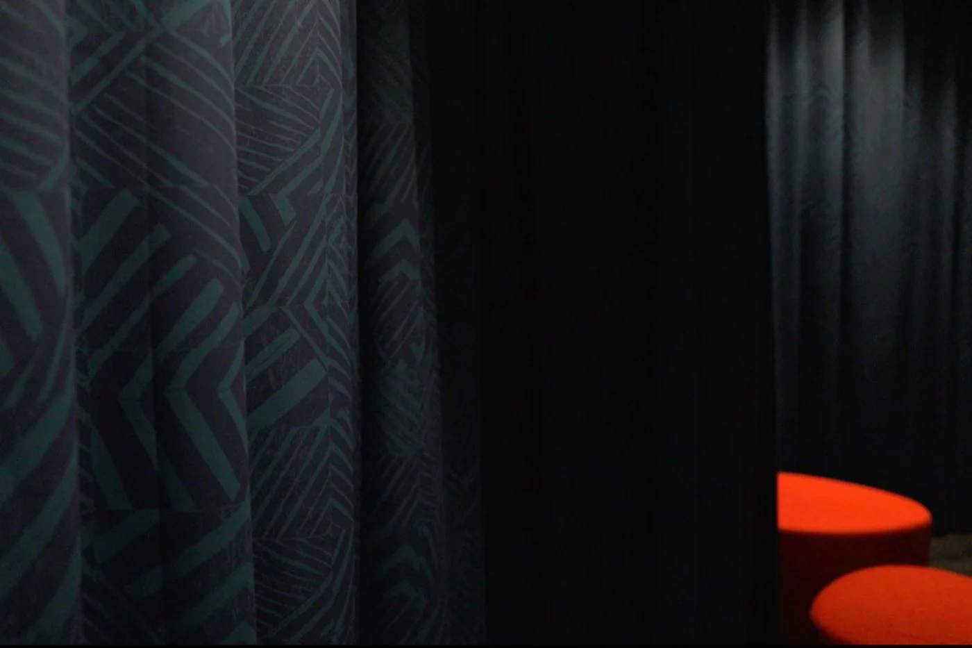 Close up of a patterned curtain within an informal gallery space. It is a dark blue and green geometric style pattern.