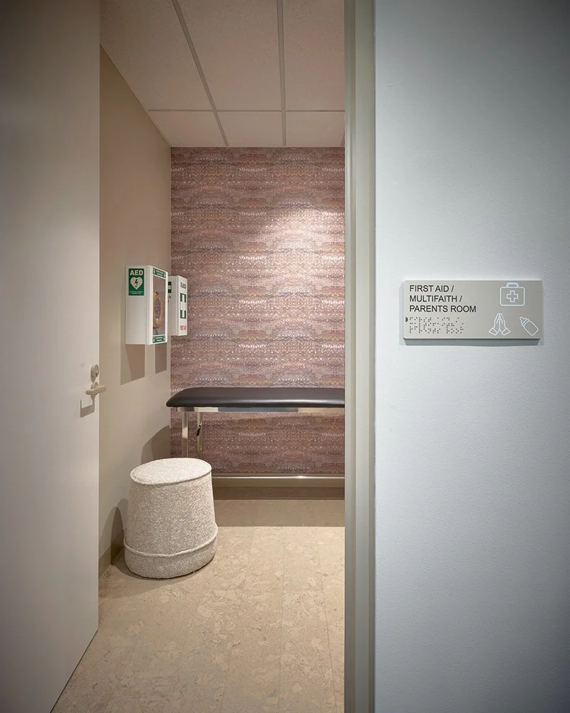A view into a first aid, multifaith and parents room within an office environment. On one wall there is floral patterned wallpaper in earthy tones featuring small bush flowers used in 'bush medicine' in Aboriginal culture.