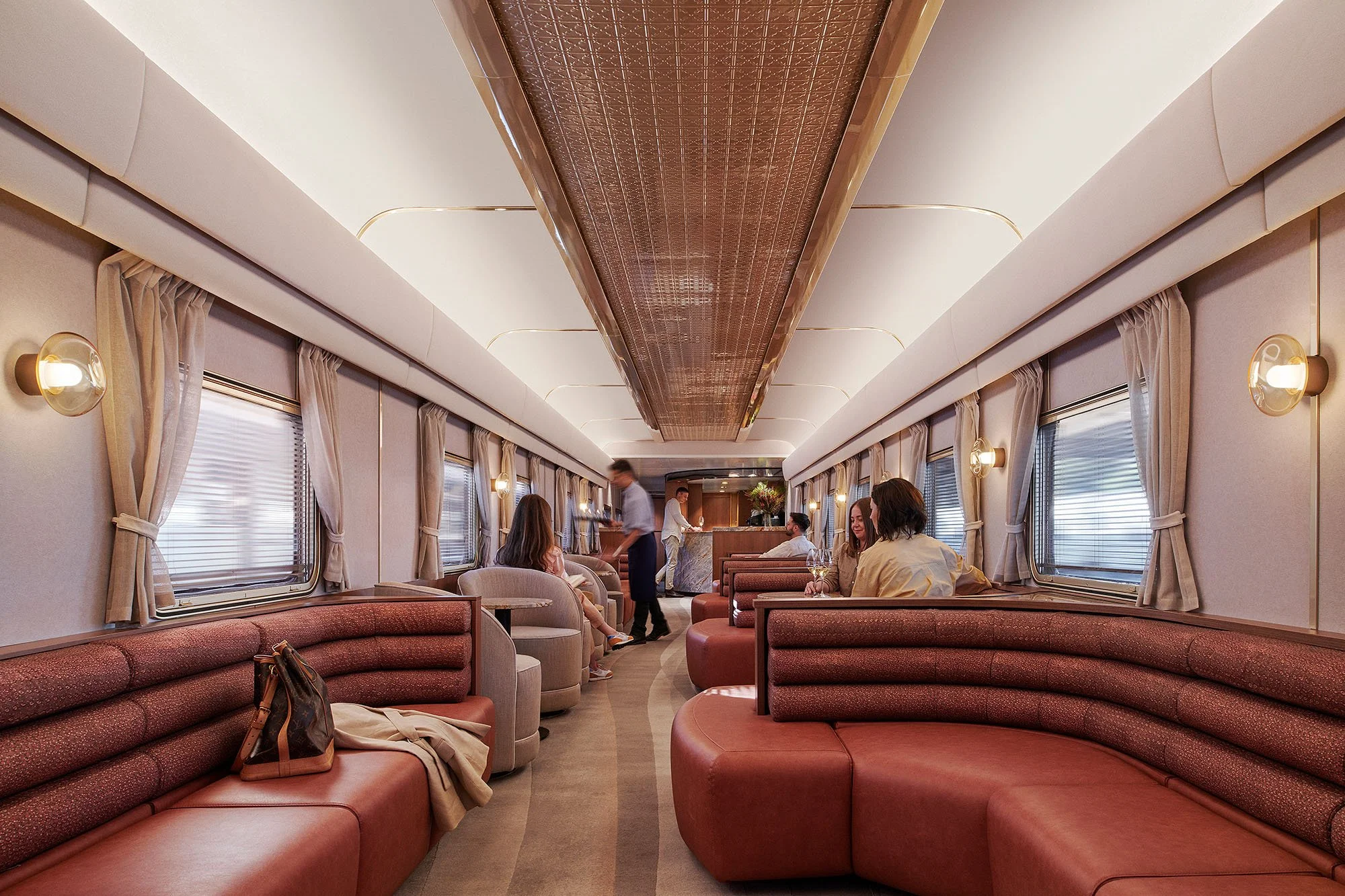 Banquette and booth seating within the Journey Beyond luxury train carriage, featuring upholstery in deep red and terracotta tones alongside more neutral greys, creams and gold accents.