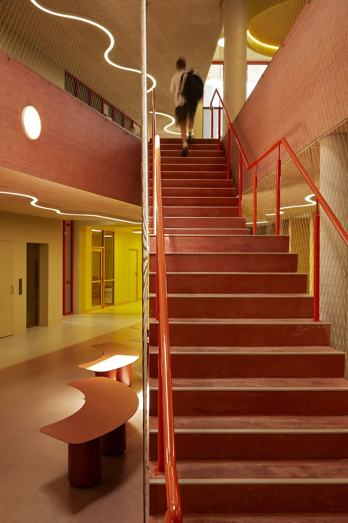 Texture, colour and light play together in the halls and staircases of Auburn High School. Bright yellow walls, shiny orange hand rails, terracotta printed acoustic panelling and sculptural lighting create a warm and energising space for students.