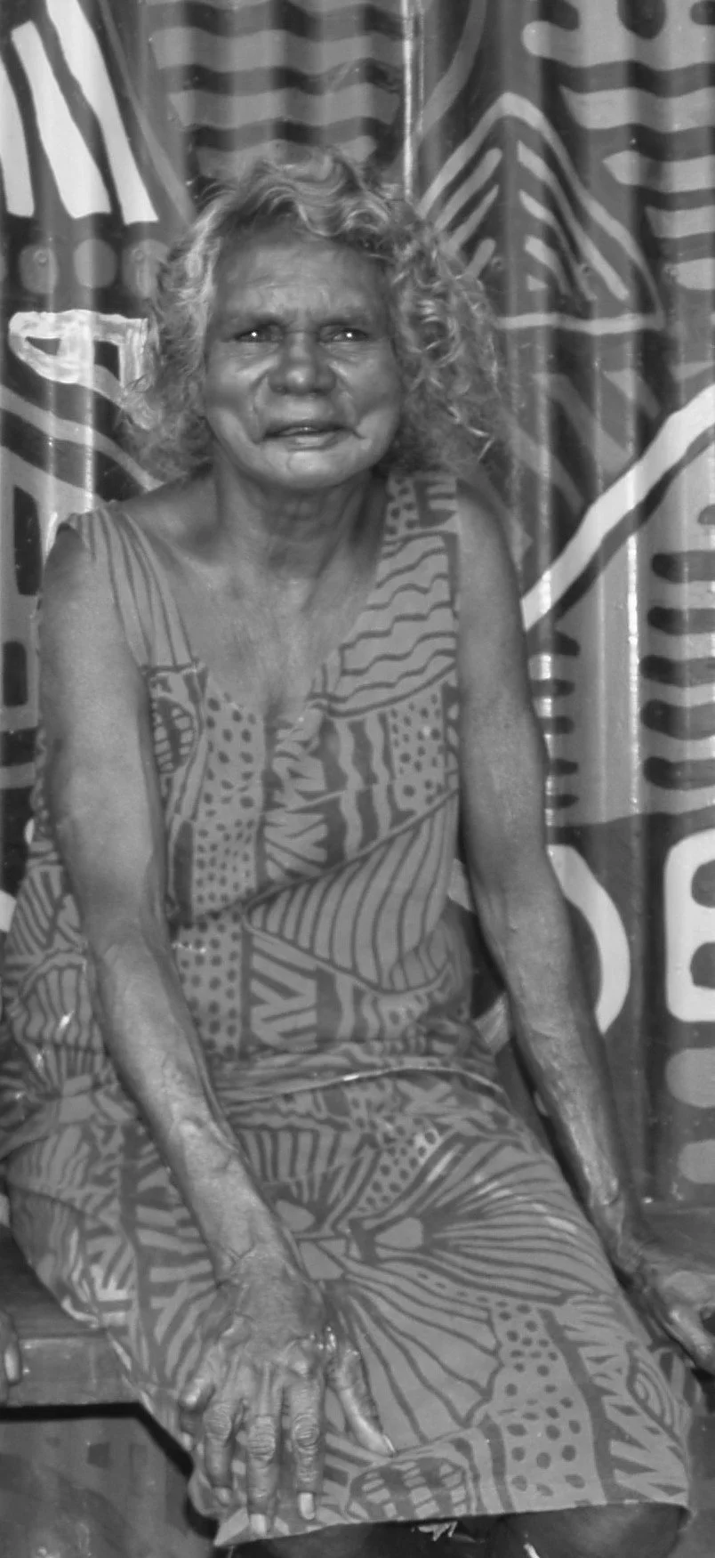 Black and white portrait of an Indigenous woman with a patterned painted background.