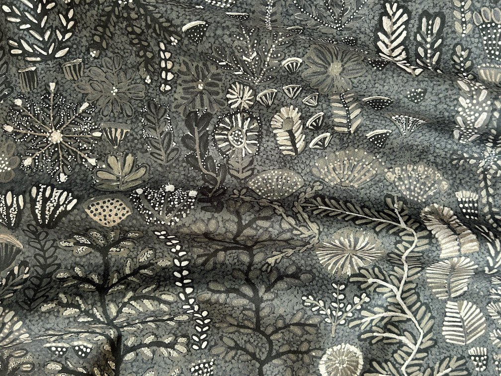 Fabric laid out with soft folds printed with Indigenous-designed floral pattern in colours of green, white, black and grey.