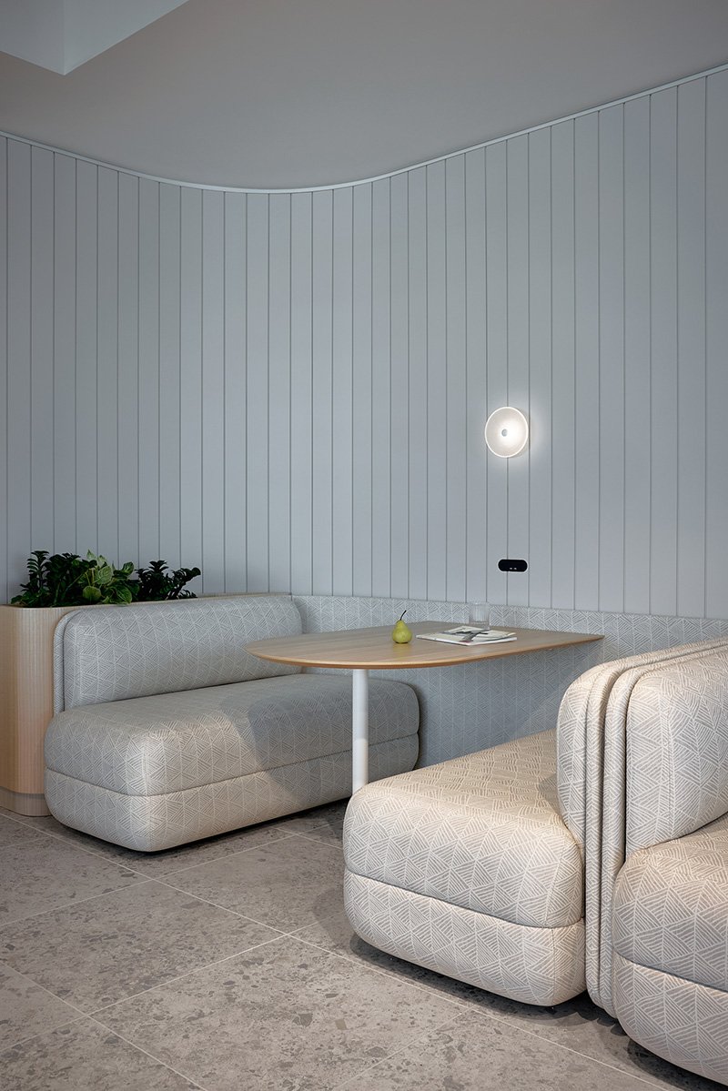 Booth seating upholstered in a grey and white patterned fabric, with matching fabric wall panelling, tiled floors and indoor plants. The office setting is serene and comfortable.