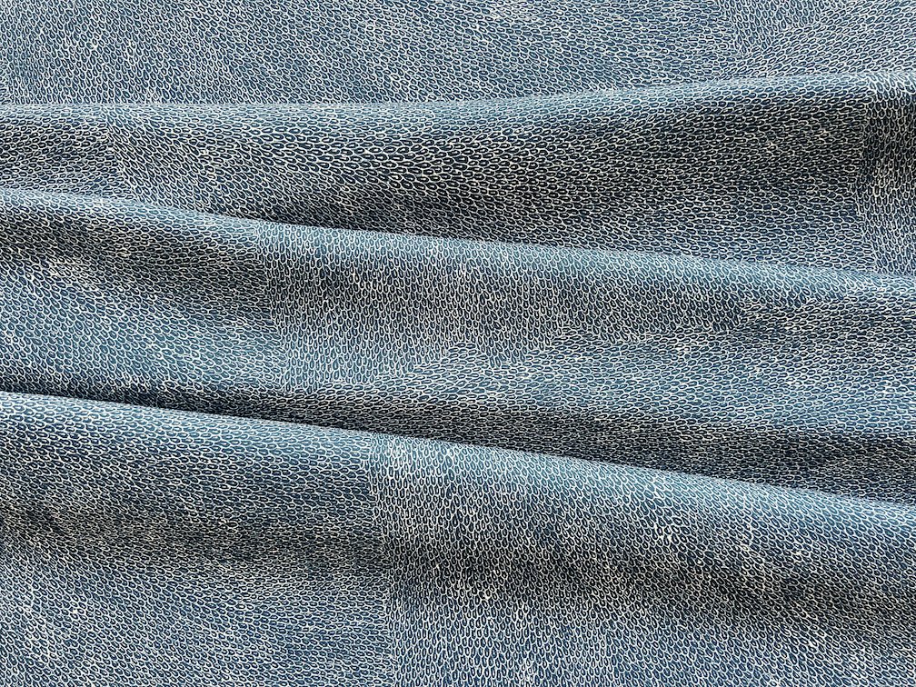 Fabric laid out with soft folds printed with First Nations design of small seeds of white on dark blue