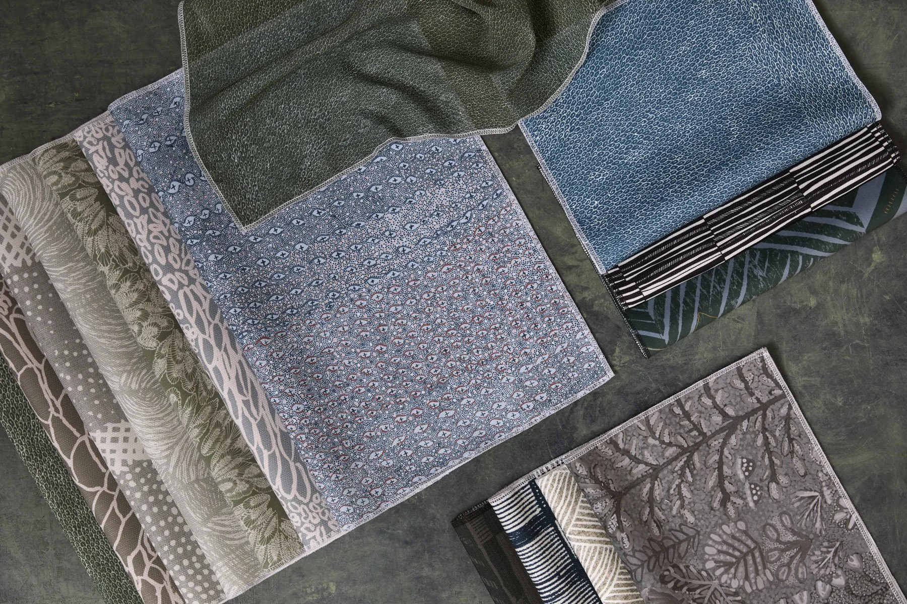 Various patterned fabrics laid out and folded on a flat surface, in moody blues and greens.