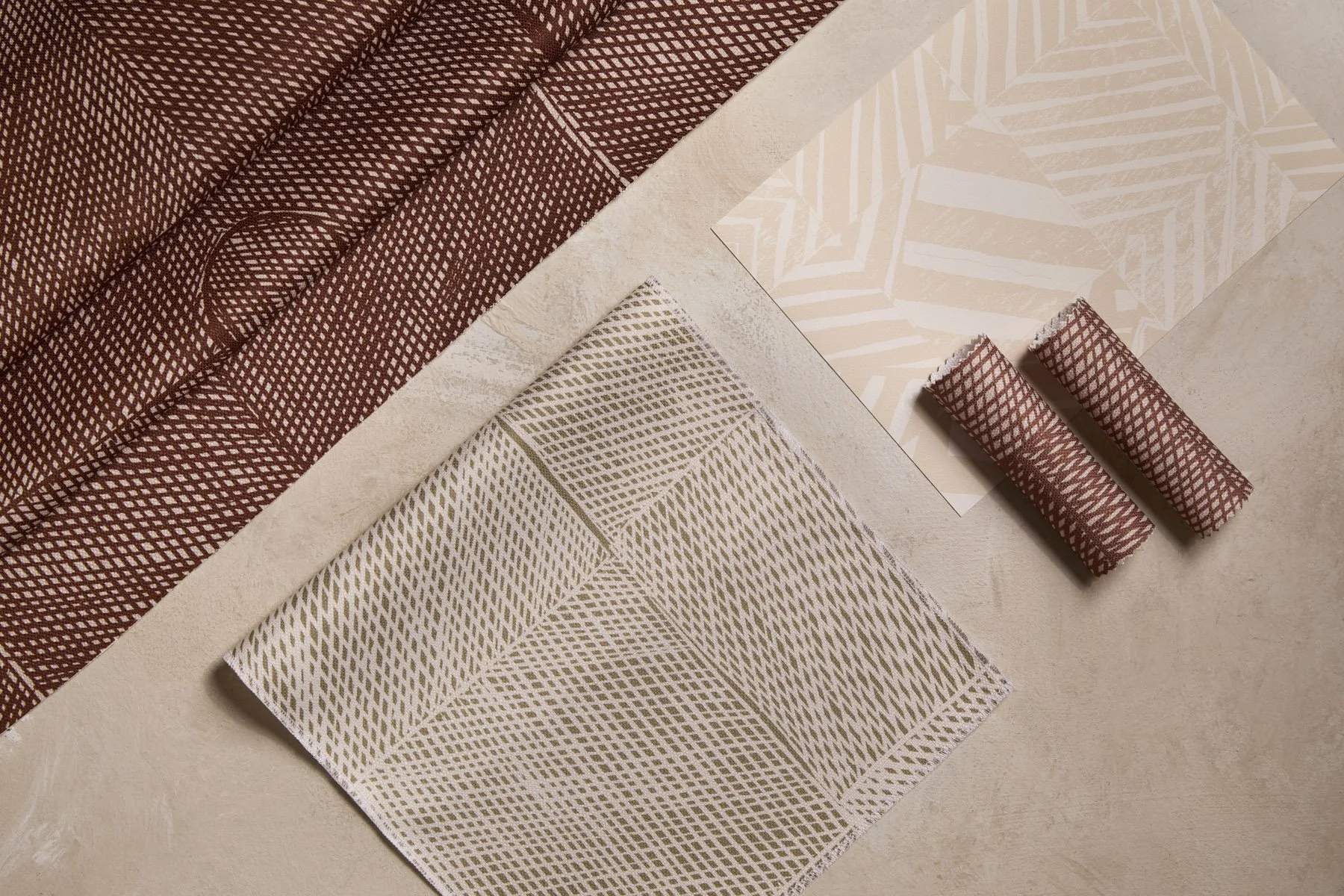 Various patterned fabrics and wallpapers laid out and folded on a flat surface, in brown, khaki and sand colours.