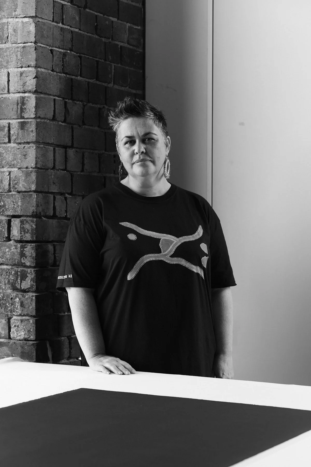 Black and white portrait of an Indigenous woman with a brick wall in background.