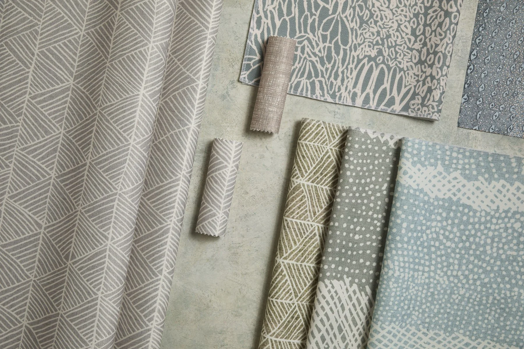 Various patterned fabrics laid out and folded on a flat surface, in blue, green and grey colours.