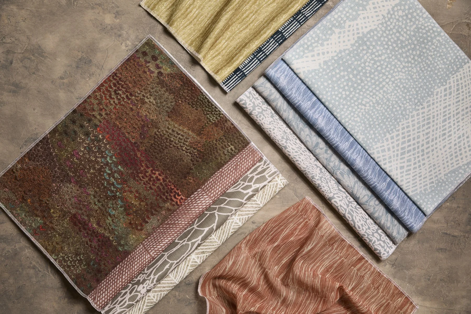Various patterned fabrics laid out and folded on a flat grey surface, in earthy as well as brighter colours.