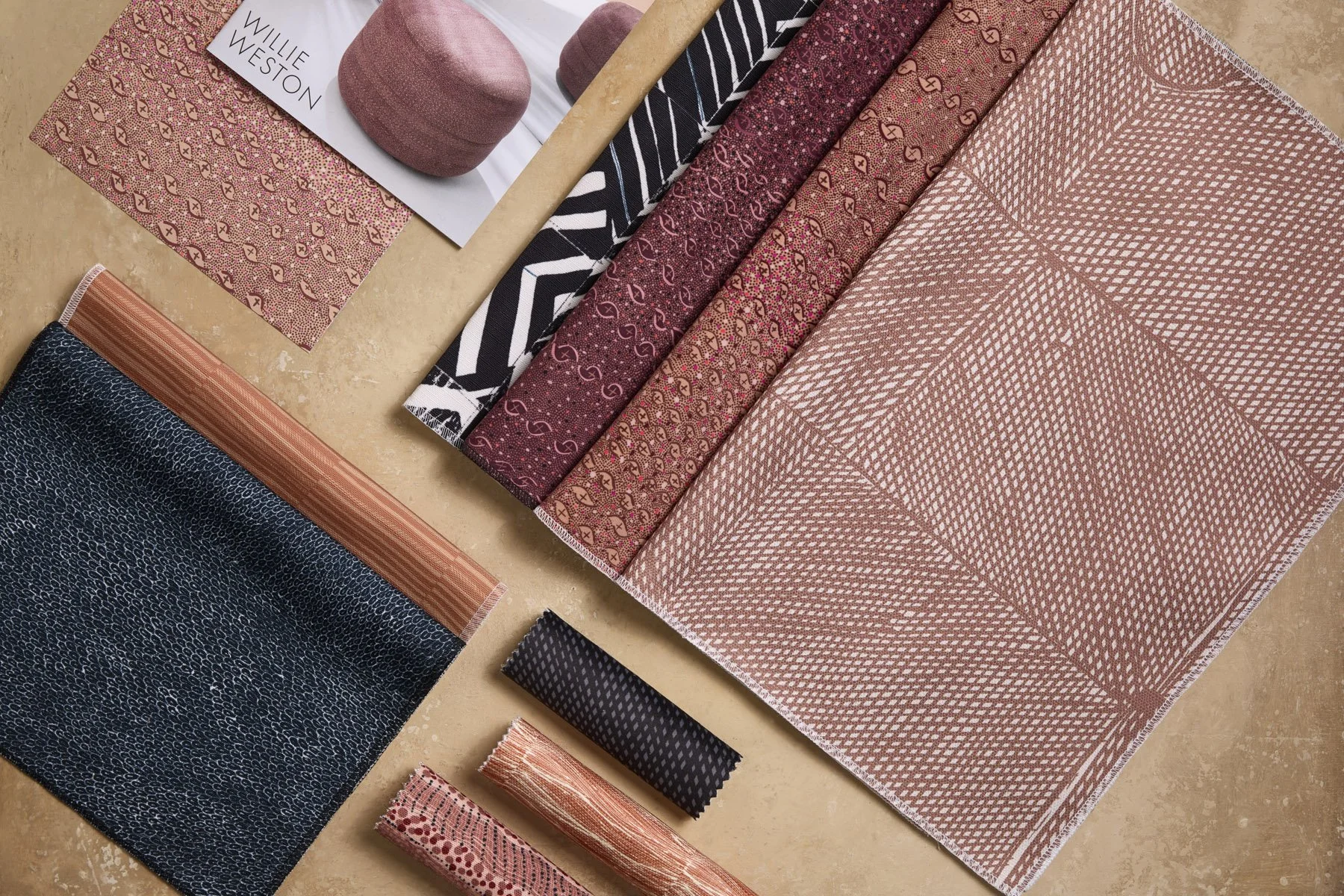 Various patterned fabric samples laid out and folded on a flat surface, in terracotta, plum and black colours.