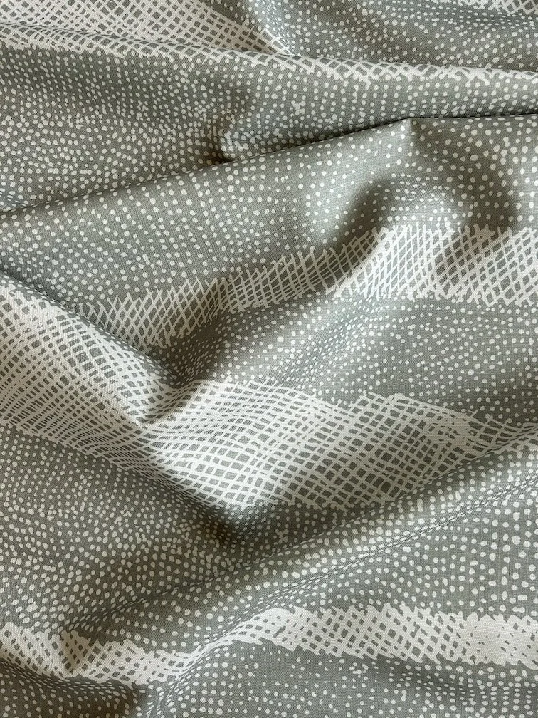 Fabric laid out with soft folds printed with First Nations artwork in a pale green colour with white cross-hatched lines and dots.