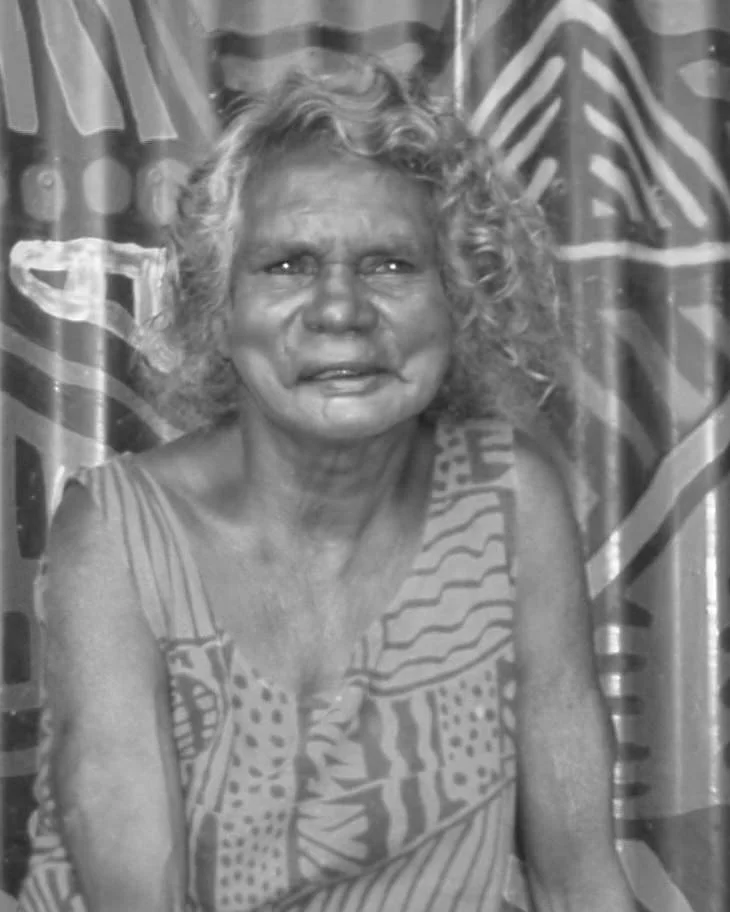 Black and white portrait of an Indigenous woman with a patterned painted background.