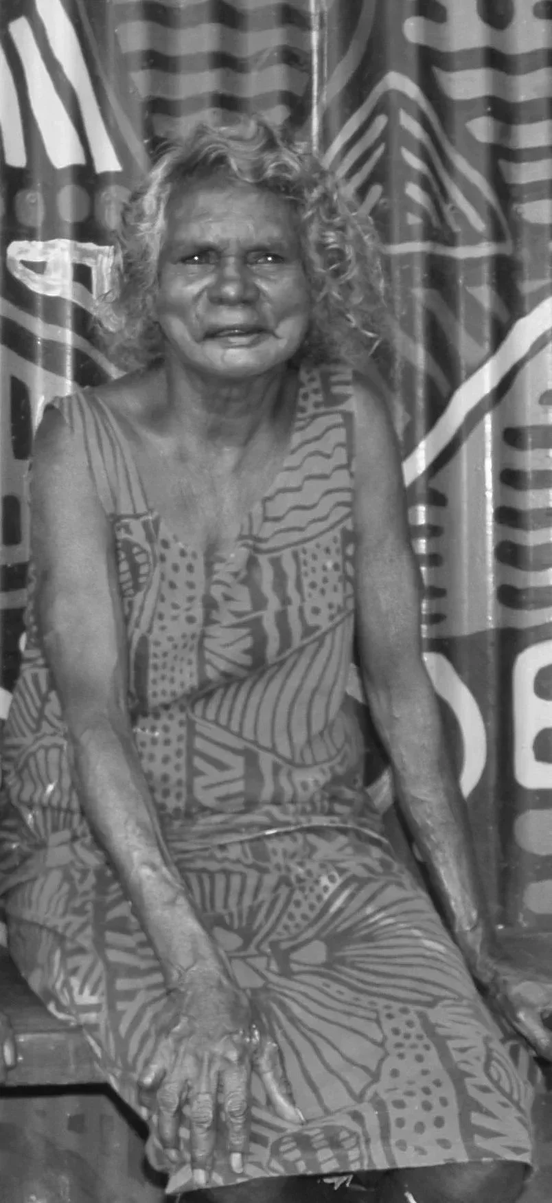 Black and white portrait of an Indigenous woman with a patterned painted background.
