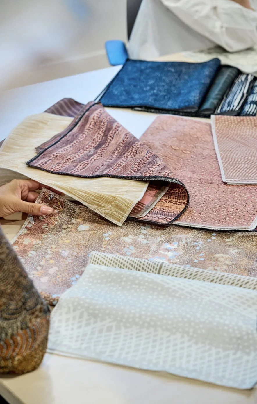 Various fabric samples and swatches spread on a table, with a hand holding a fabric sample on the left side.