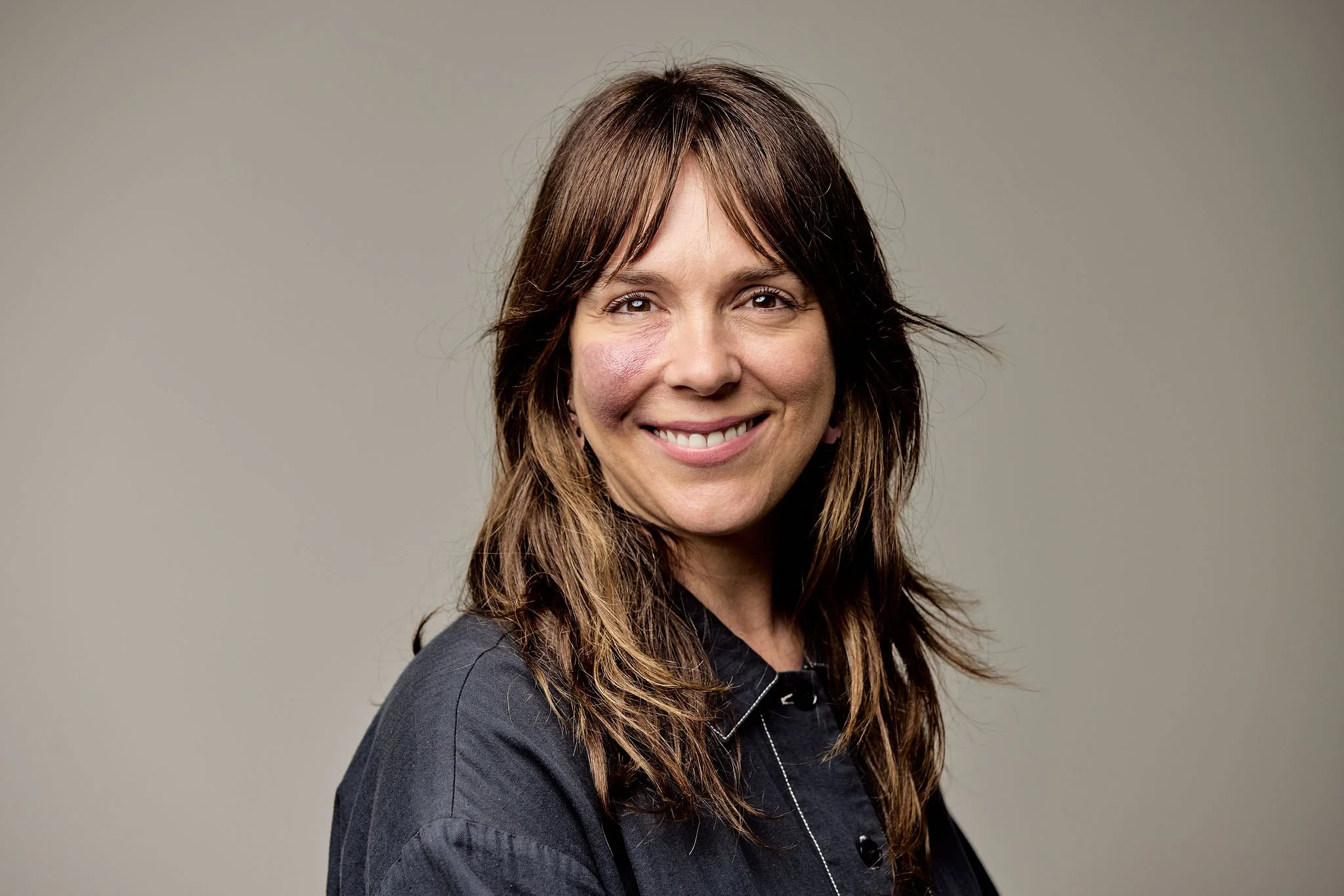 A woman with long brown hair, smiling, wearing a black jacket.