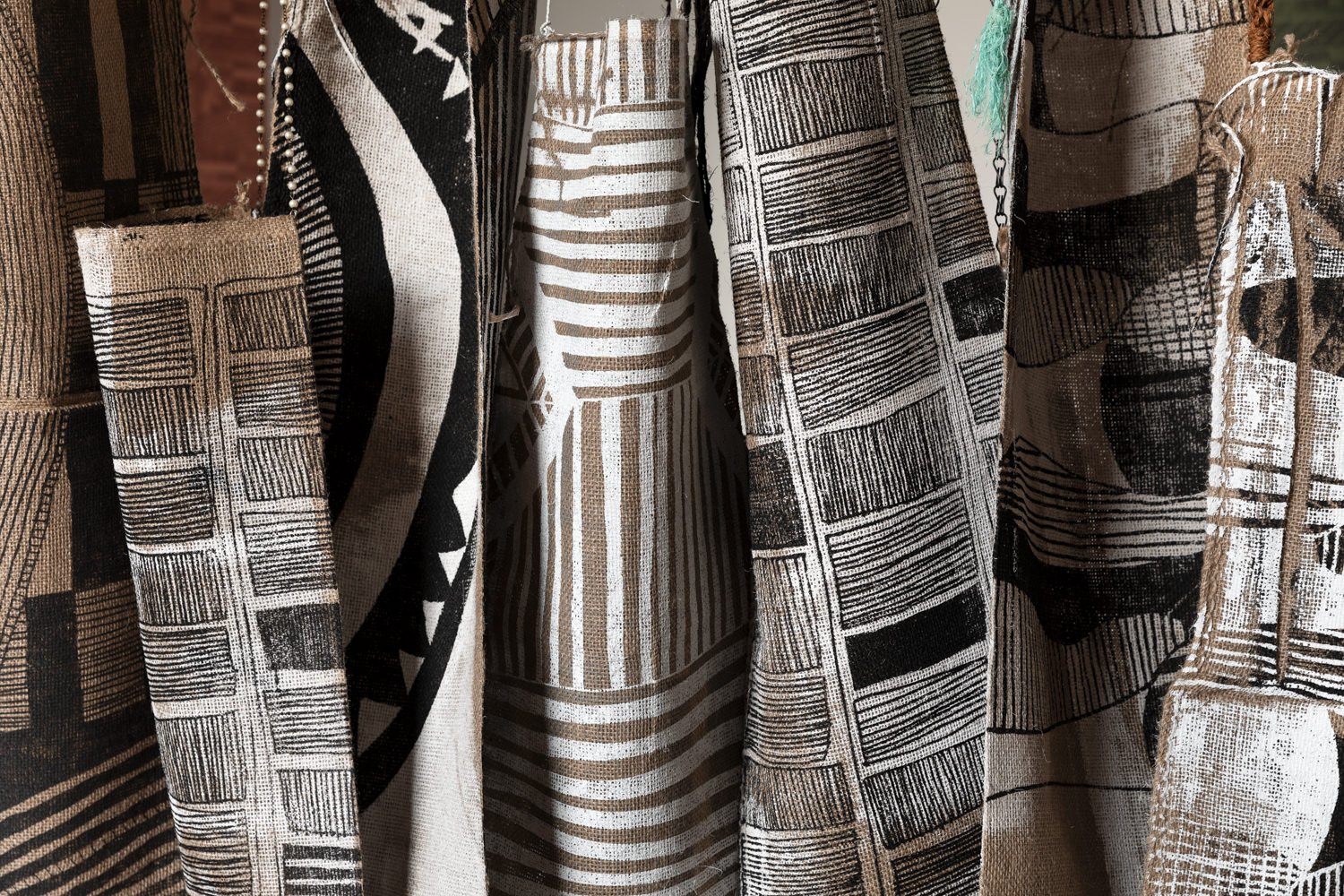 A close-up of jute bags hanging together that have been screen-printed with geometric patterns using ink and reflective ink. The bags are from Lisa Waup’s Holding Country III, 2023-2024 project.