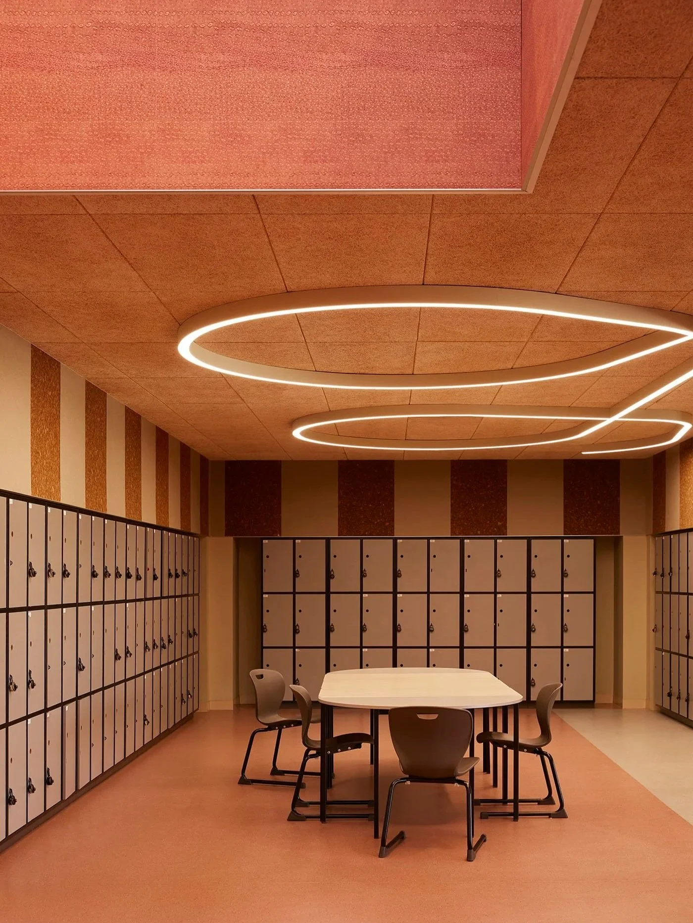 The student locker room at Auburn High school features a textural cork ceiling and sculptural ceiling light, terracotta toned printed acoustic panelling and a communal table and chairs - which create a warm and modern space for students to hang out.