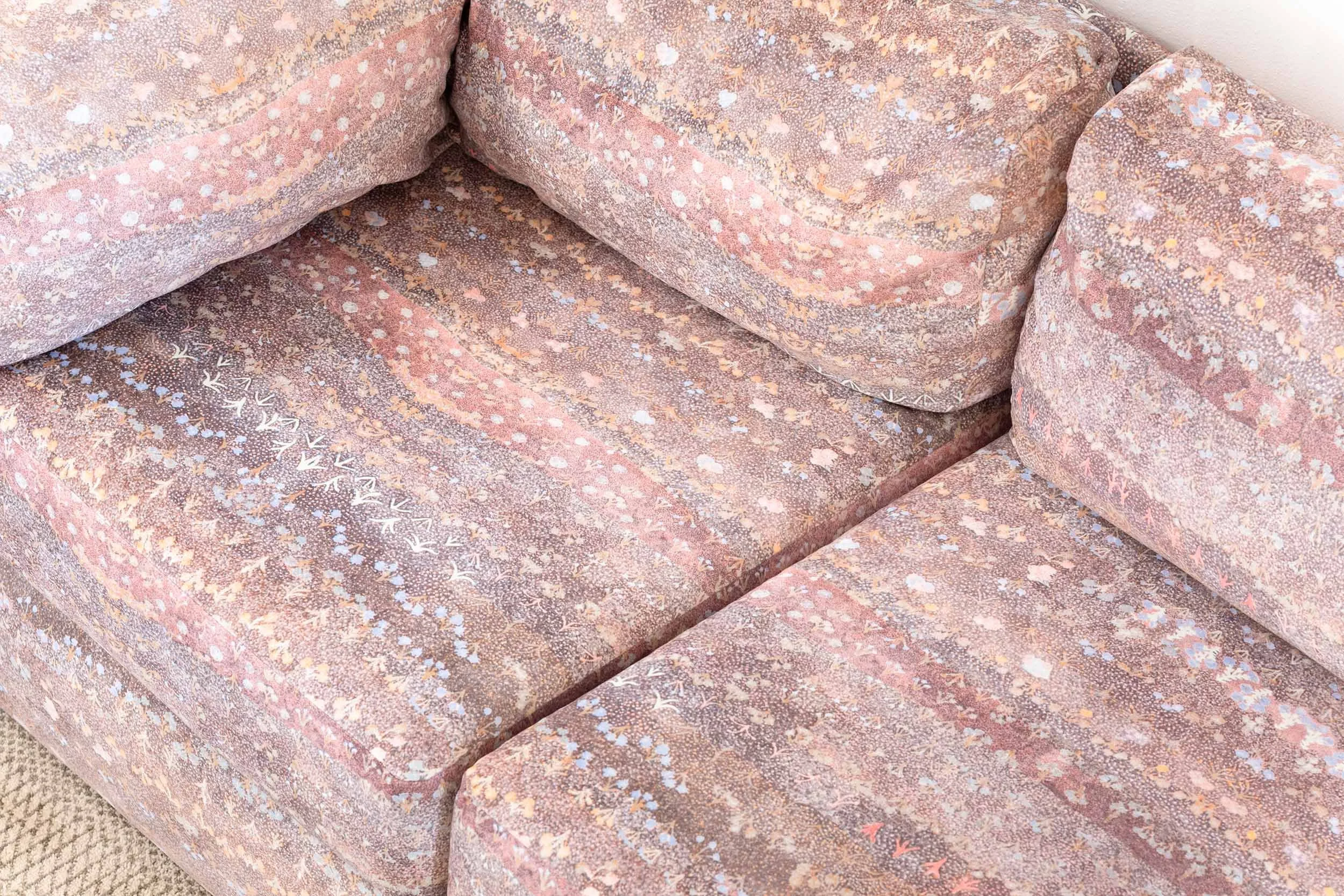 Cropped image of upholstered sofa featuring First Nations design with colours of brown, plum, mauve, yellow, pink