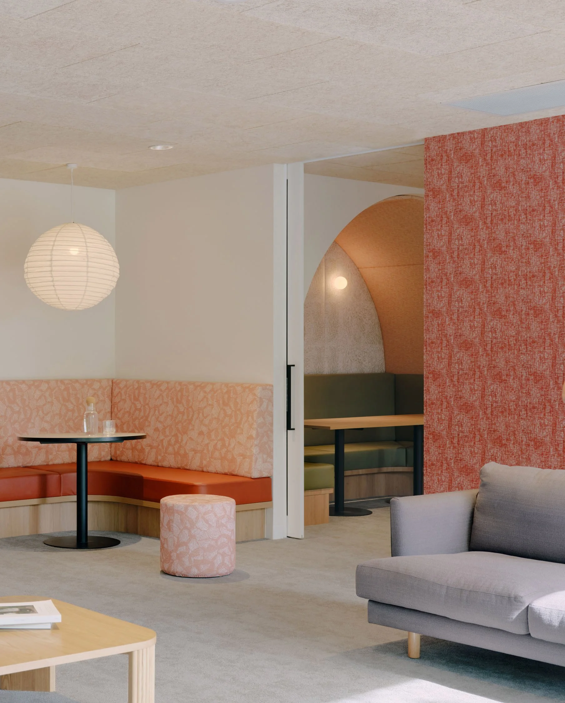 A breakout space within Melbourne Indigenous Transition School featuring upholstered banquet seating, ottomans and wall panelling - featuring prints in complimentary tones of peach and rust.