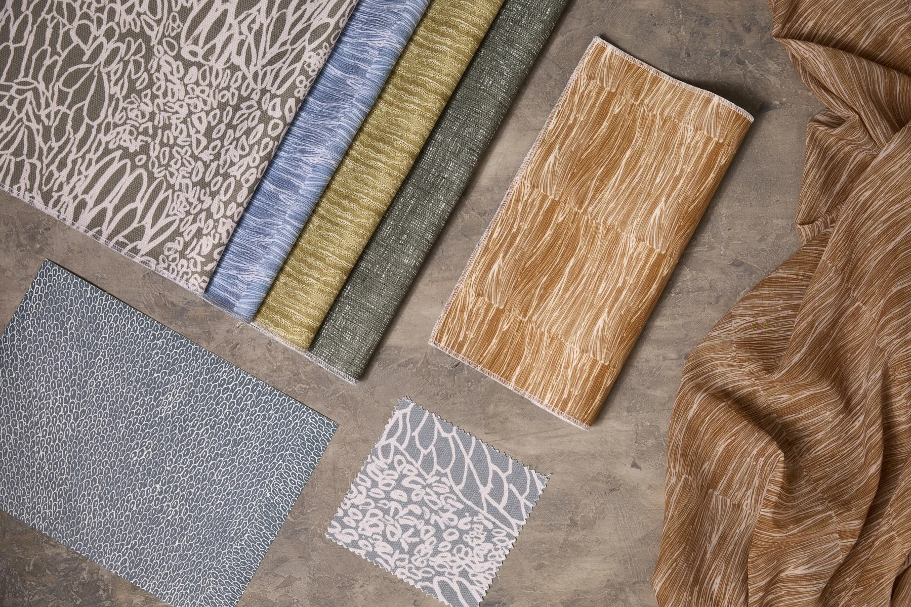 Various patterned fabrics laid out and folded on a flat surface, in fresh blue, green and gold colours.