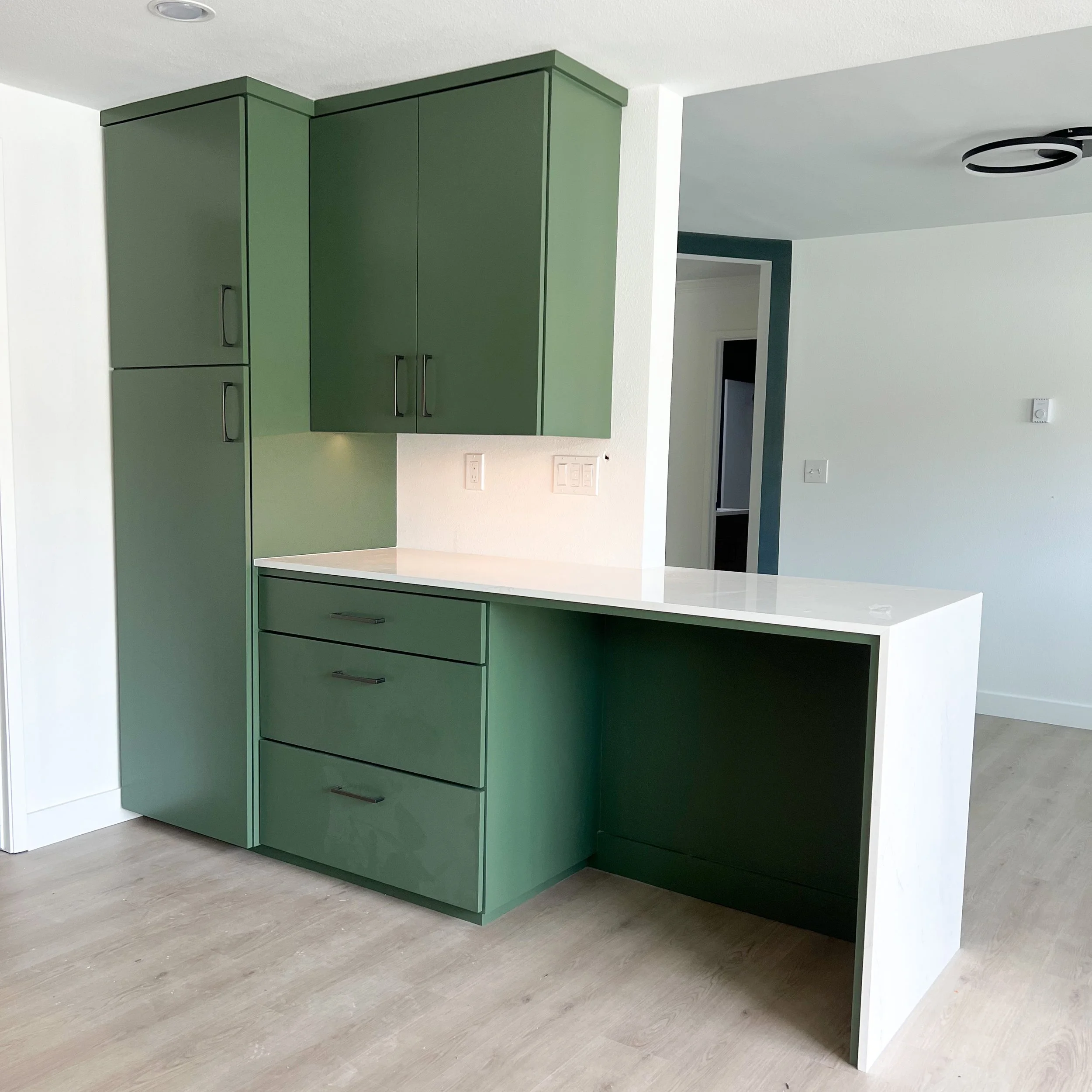A wall was shortened to give more of an open feel to both the kitchen and dining areas, and this custom cabinetry was created to provide much needed storage, and functionality as a casual dining + office area.  The deep green paint and streamlined ha