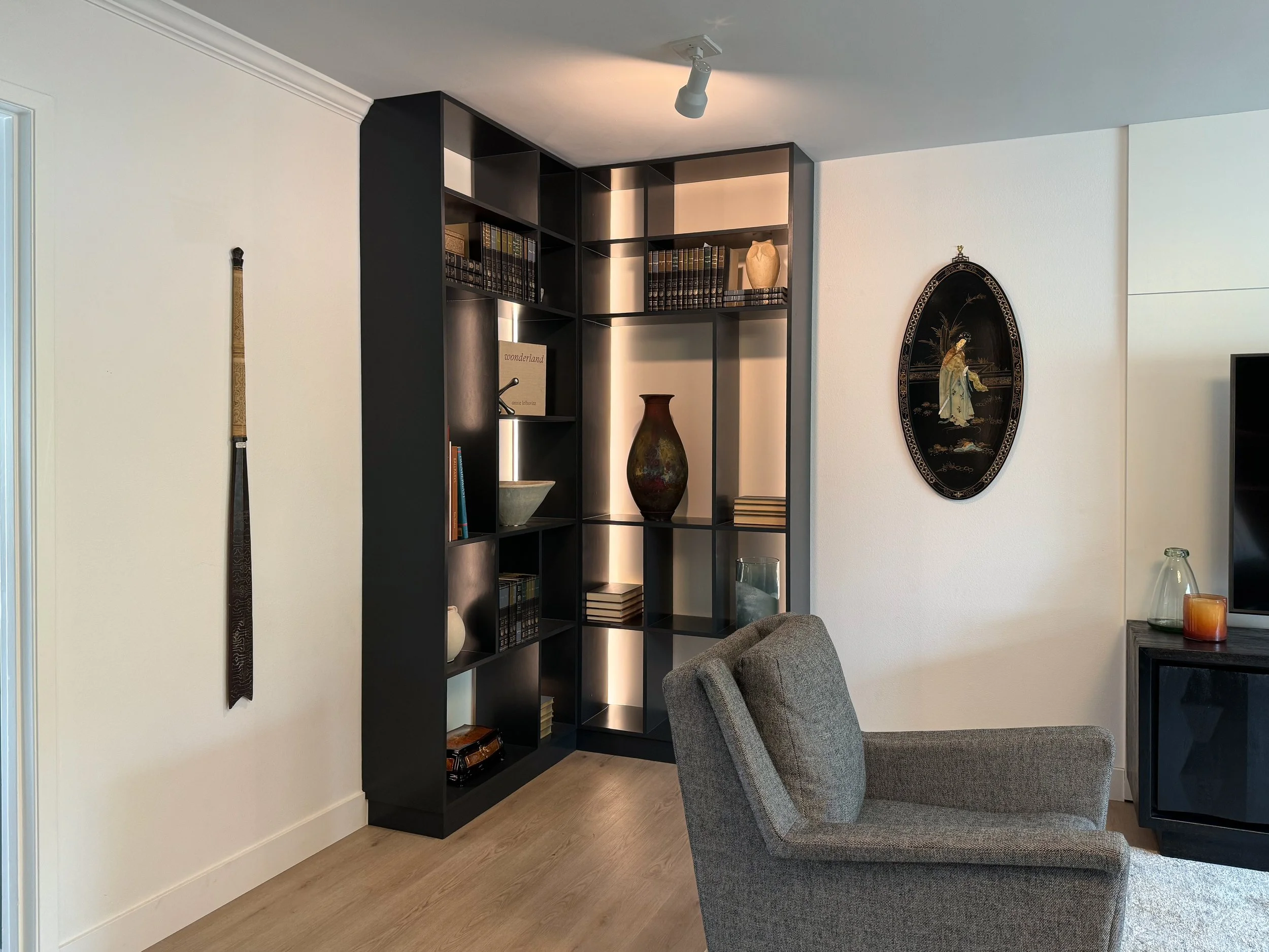 This corner bookshelf was designed to hold collected art and other items the client wanted to display, as well as creating interest and cohesion in style across the newly remodeled living room.