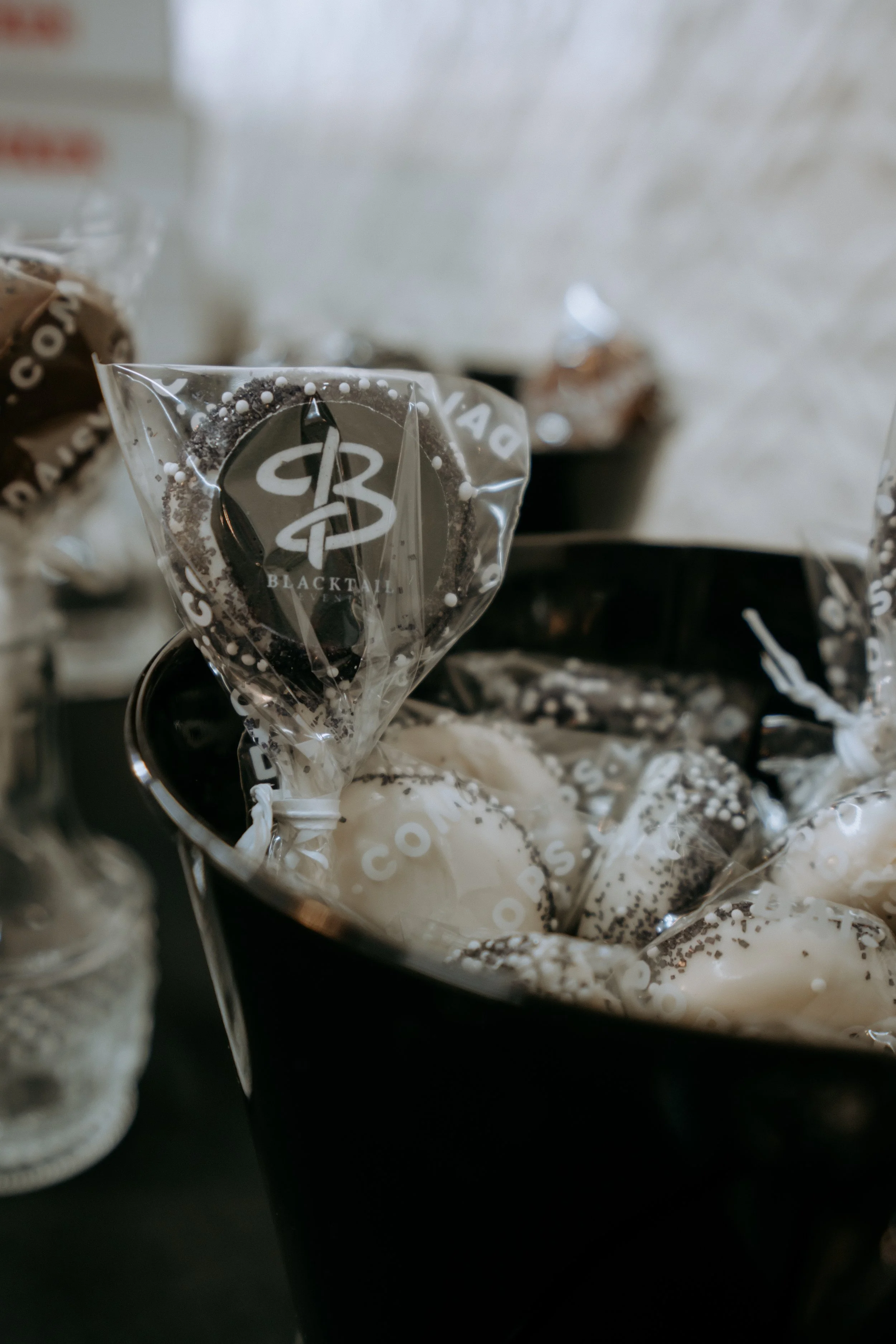 Close-up of assorted chocolates wrapped in clear plastic with black and white branding, placed in a black container.