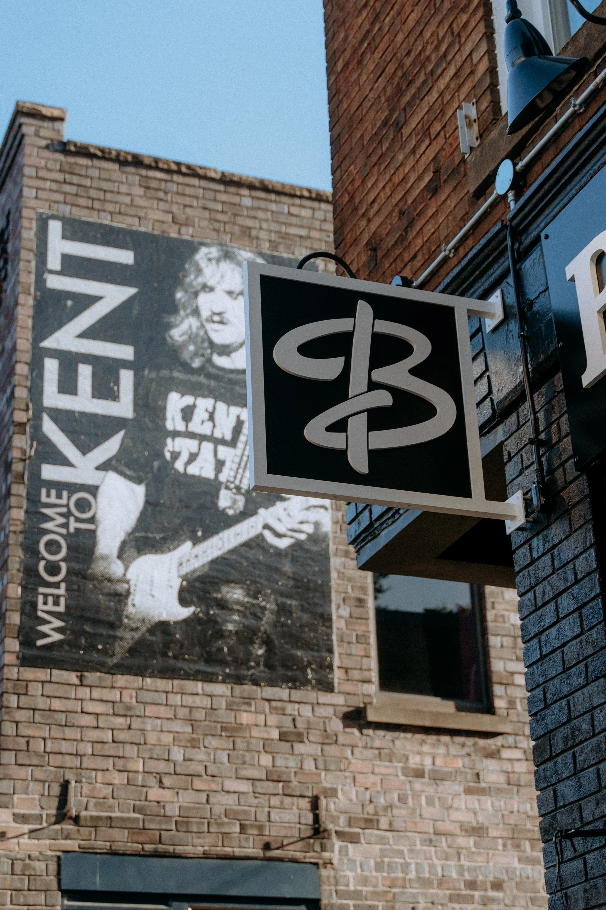 Close-up of a brick building with a black and white poster showing a person playing guitar and the words "WELCOME to Kent" in large letters.