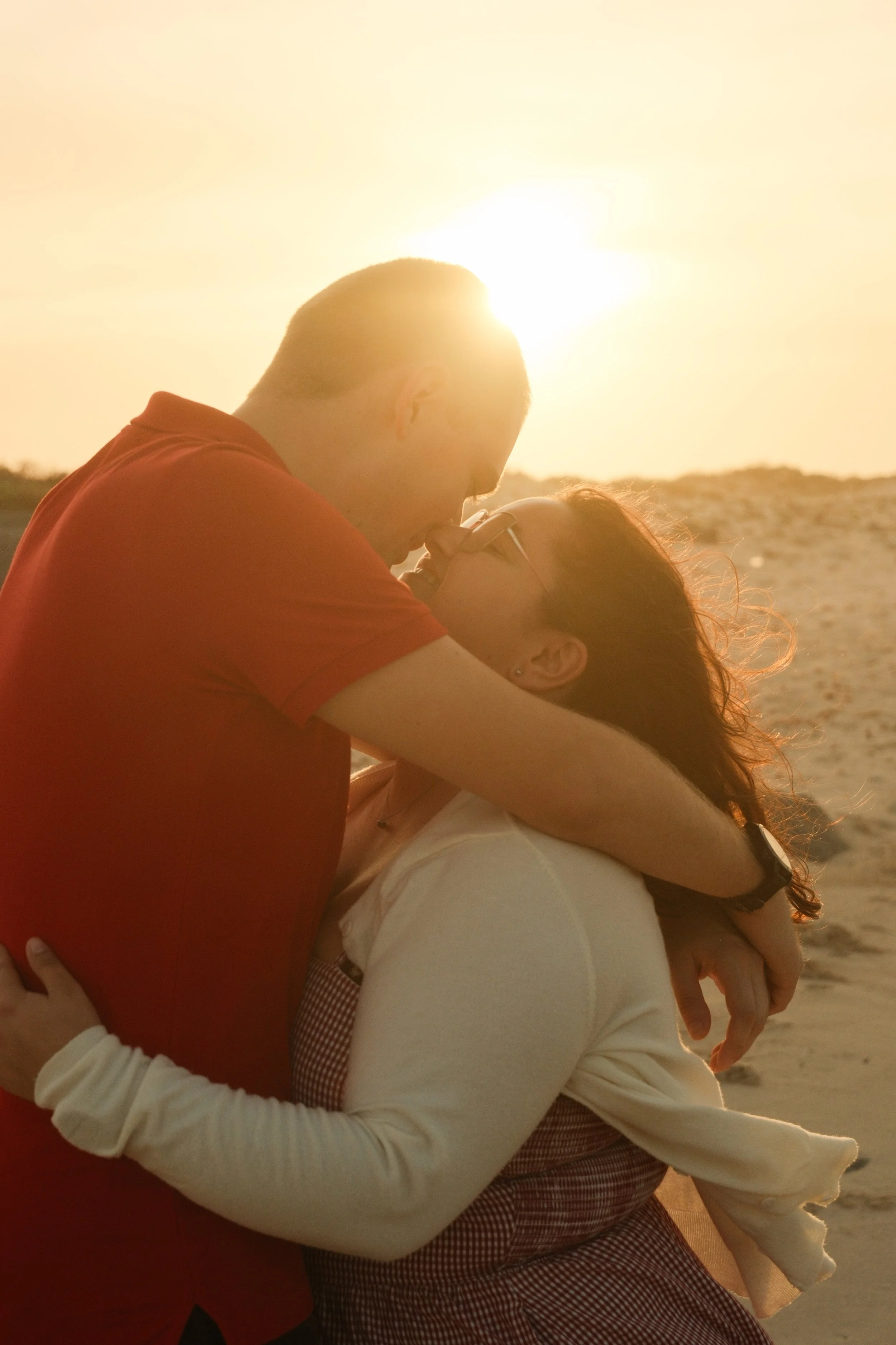 A couple embracing and kissing at sunset on a sandy beach.