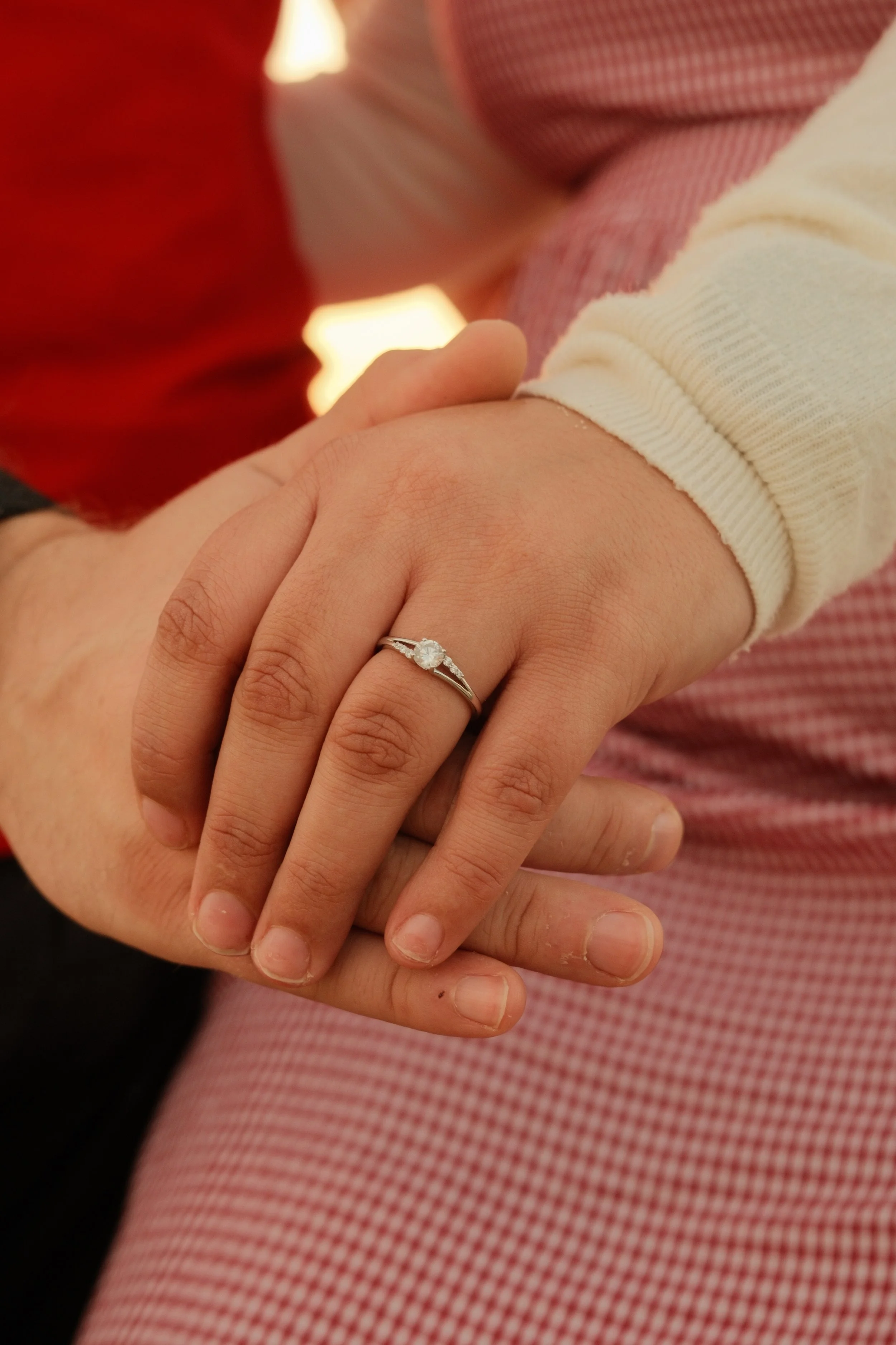 Close-up of a person's hand wearing an engagement ring with a diamond, resting on another person's hand.