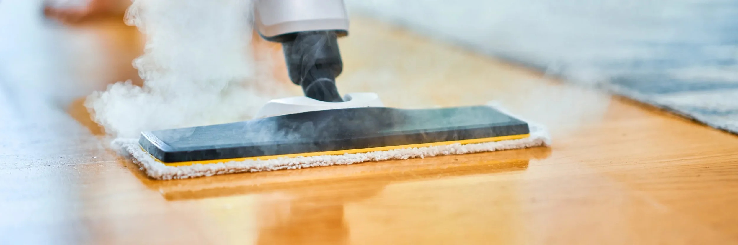 Steam rising from a steam mop as it cleans a wooden floor.