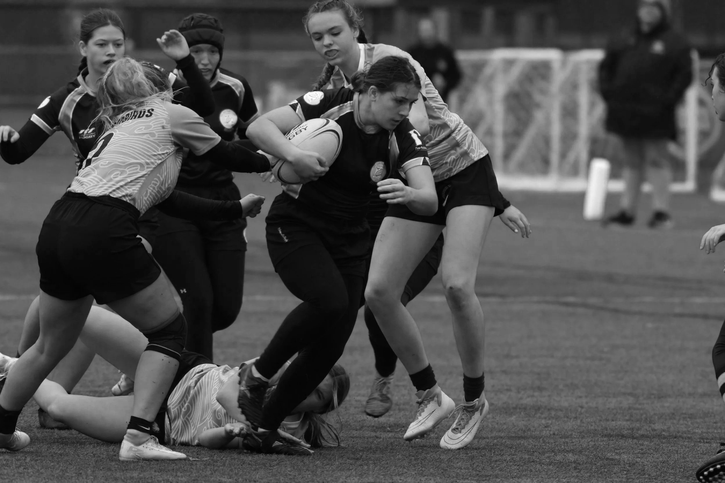 A women's rugby game in progress with players tackling, holding onto the ball, and defending on the field.