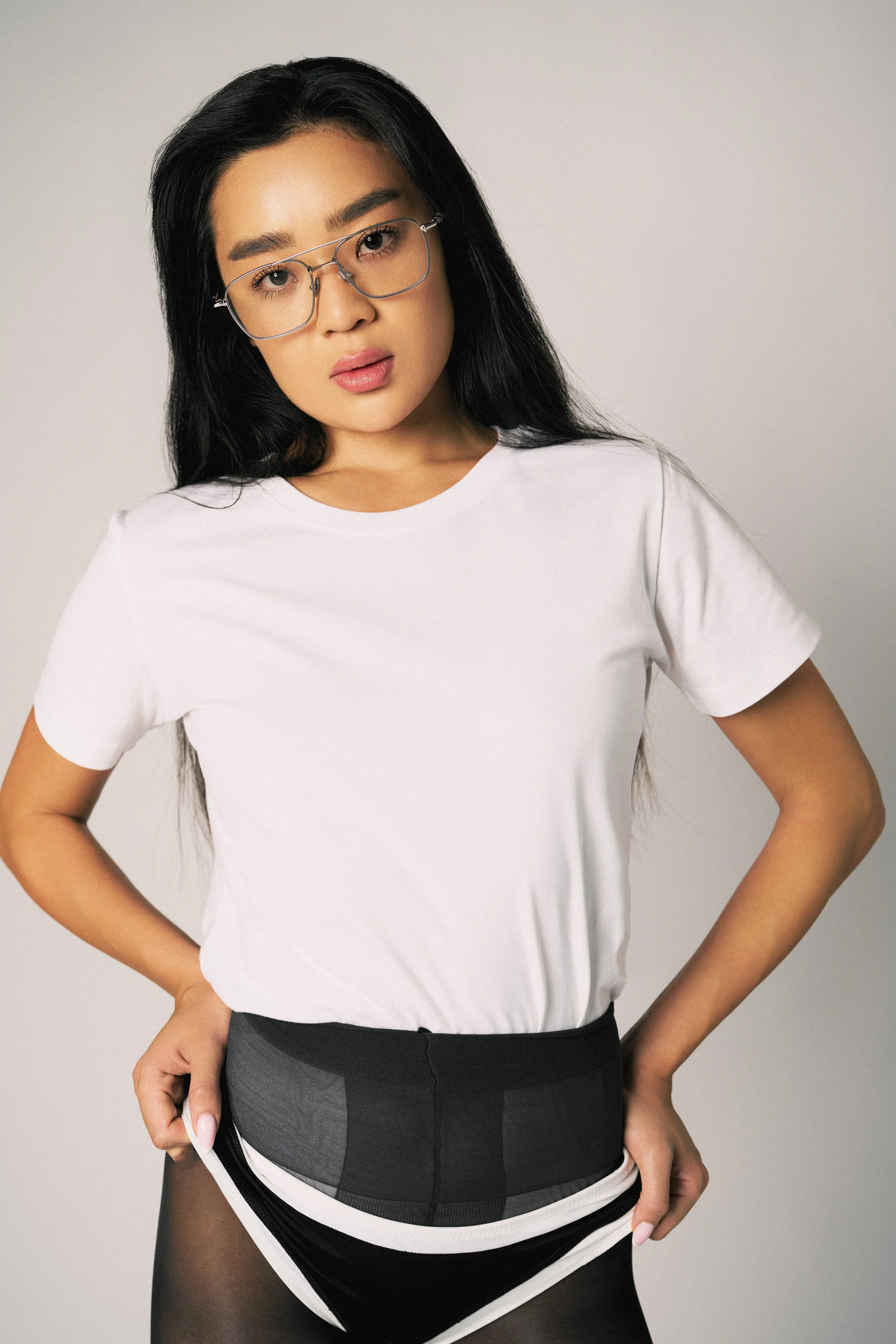 A woman with long black hair wearing glasses, a white t-shirt, black shorts, and black tights.