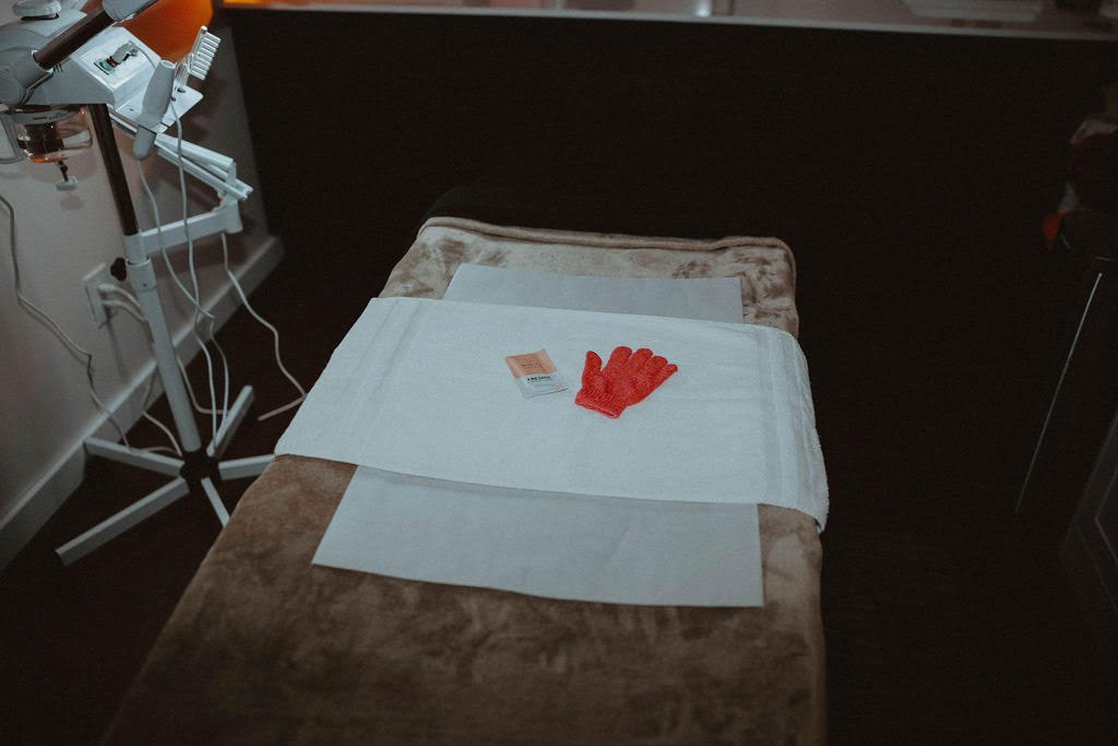 A medical examination or treatment table with a white sheet, a pair of red gloves, and a small box on top, in a clinical setting.