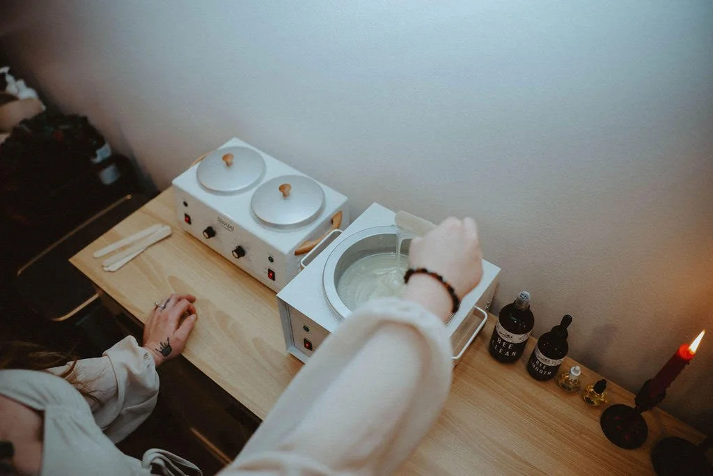Person using a small ultrasonic cleaner or jewelry cleaning device with a basin, placed on a wooden table alongside bottles labeled 'Reef Clean' and 'Reef Tooth', and a lit candle, in a cozy setting.