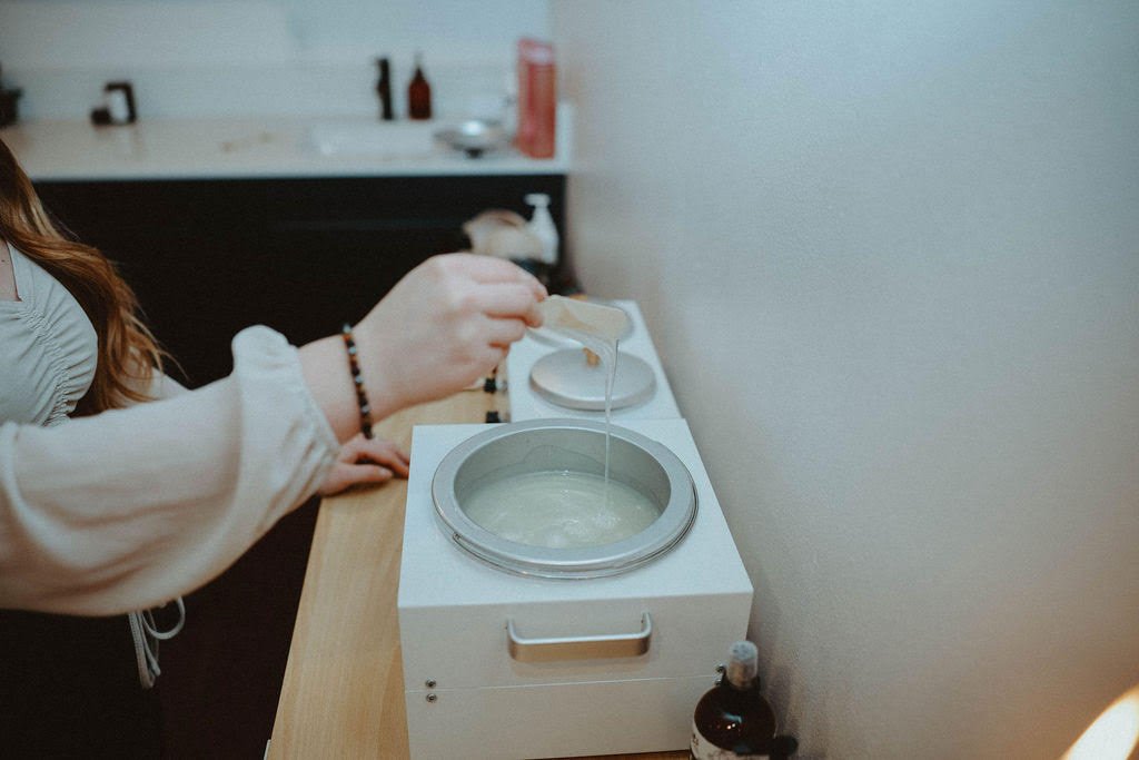 Person pouring a liquid into a hot waxing machine in a spa or beauty salon.