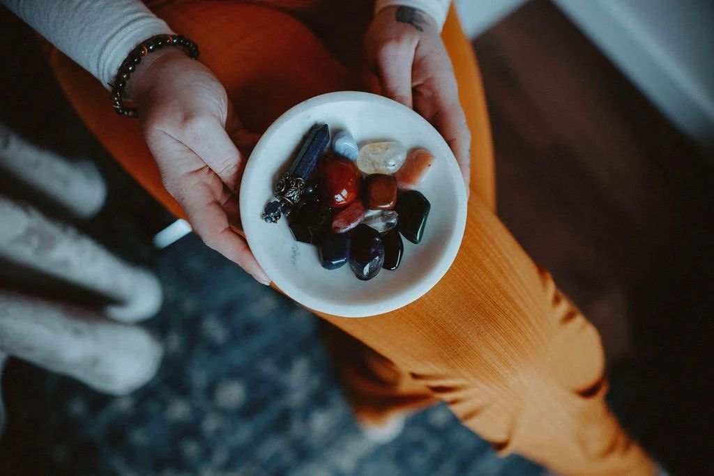 Person holding a white dish with polished stones and crystals, wearing orange pants and a white shirt.