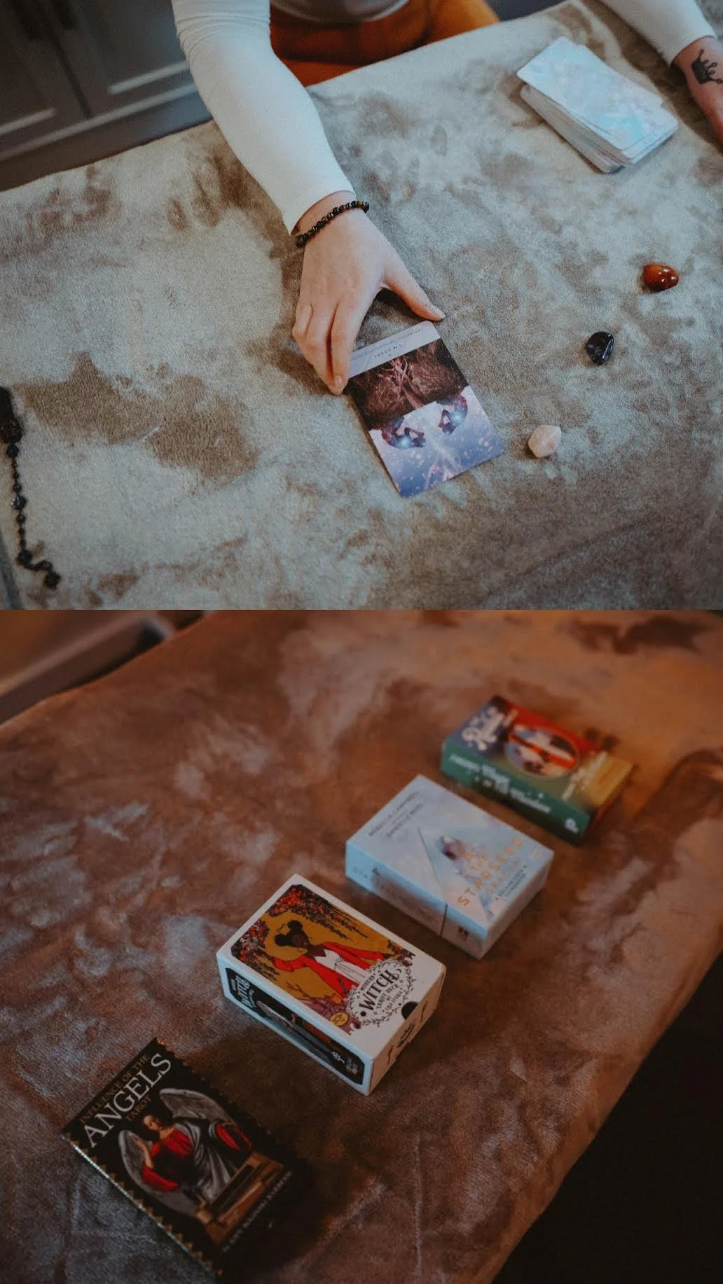 Two tables with cards and crystals. The top table has a tarot card being held by a person with a white sleeve and beaded bracelet, with various crystals nearby. The bottom table has tarot and card game boxes and a mini deck of angel cards.