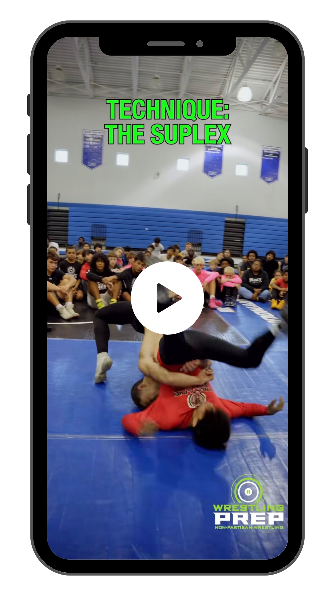 A young wrestler in a red shirt grappling with another wrestler in black on a blue mat, with a group of spectators watching in the background inside a gymnasium. The screen displays the text "Technique: The Suplex" and the logo "Wrestling Prep".