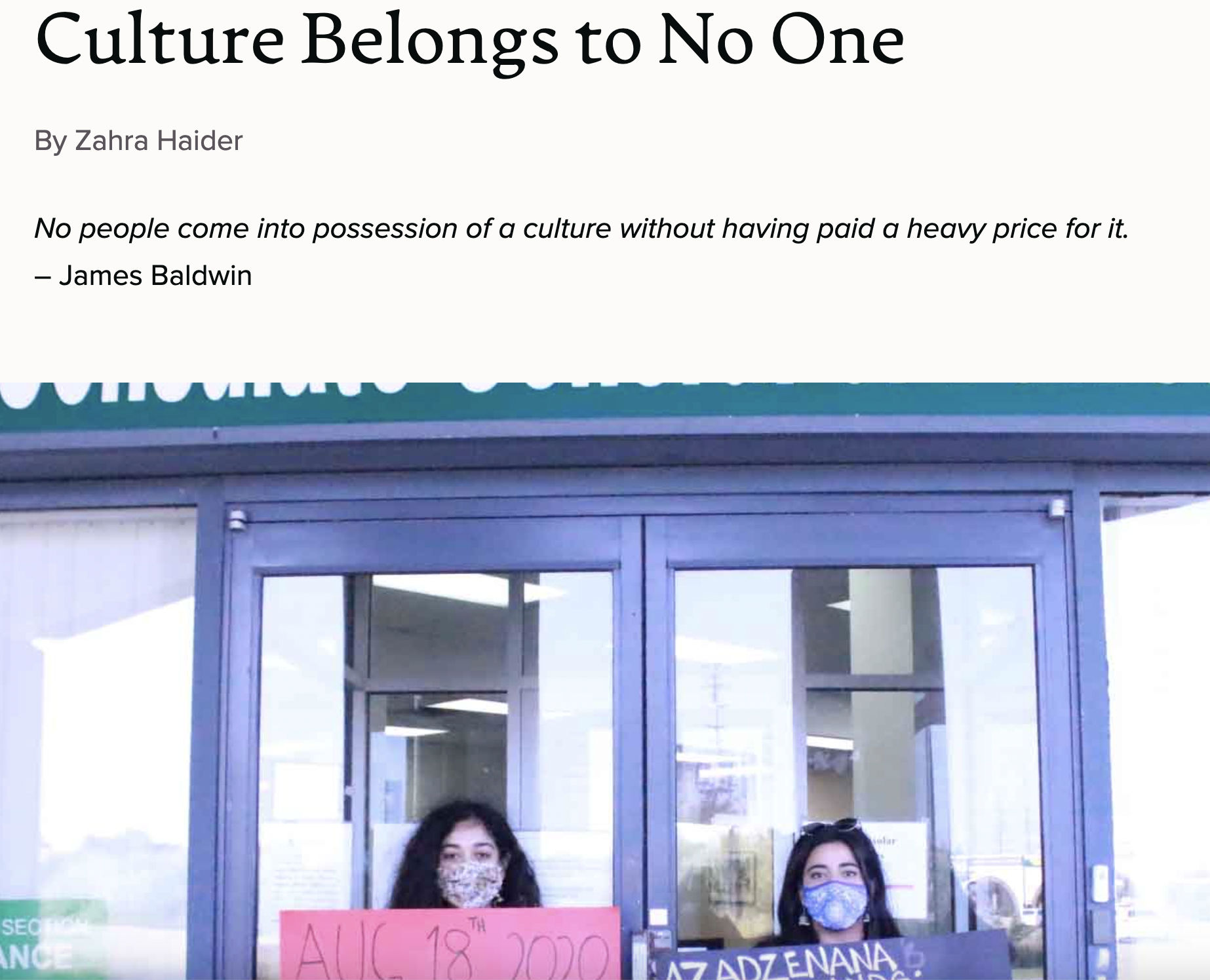Two young women wearing face masks holding signs in front of a store window with a quote about culture.