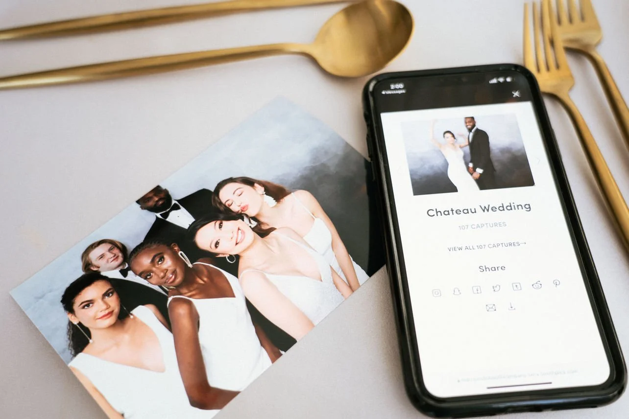 A wedding photo and a phone displaying the photo titled 'Chateau Wedding' with social media sharing options, placed on a white surface with gold and wooden cutlery around them.