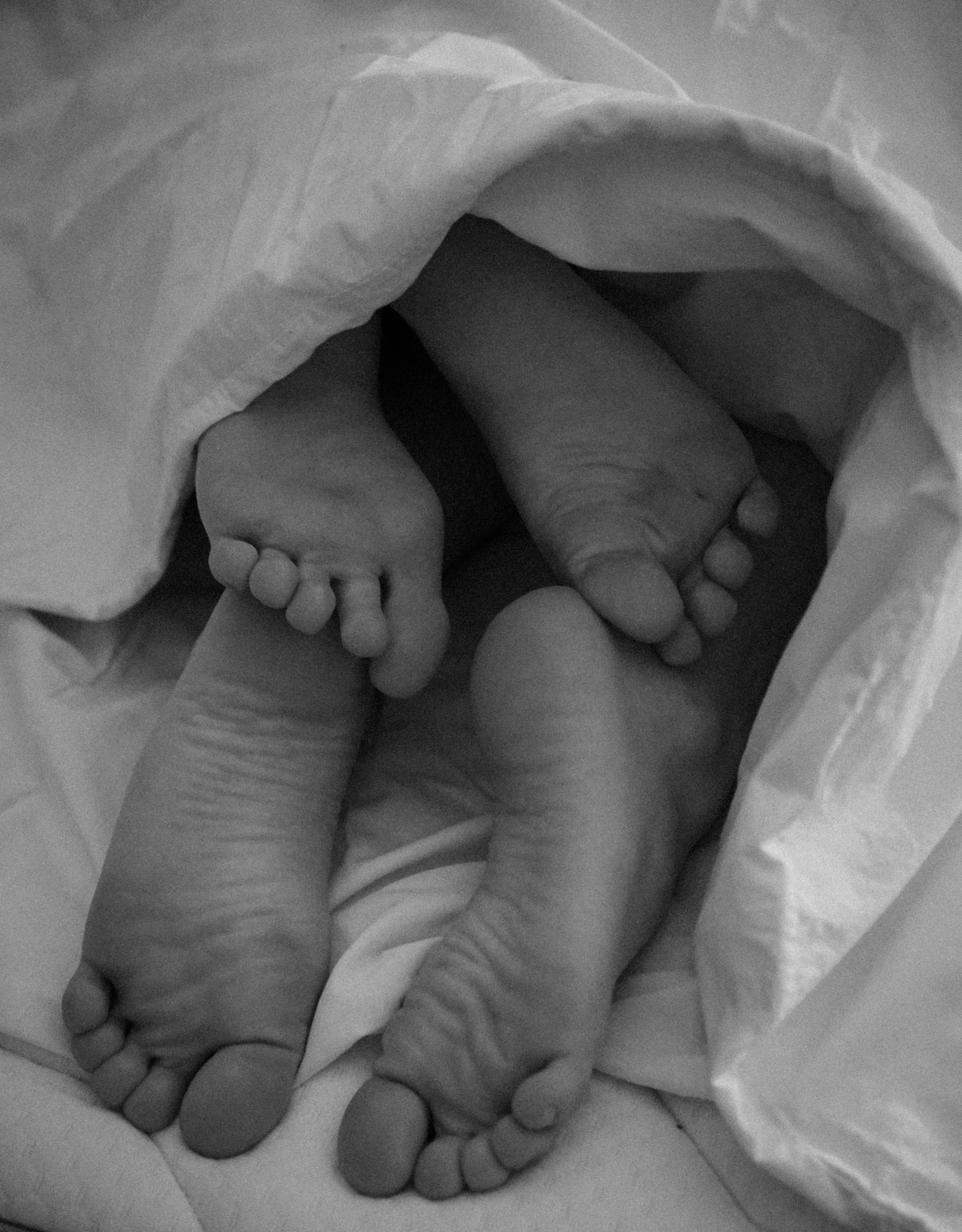 Black and white photograph of an adult's hand gently holding a tiny newborn baby's feet.