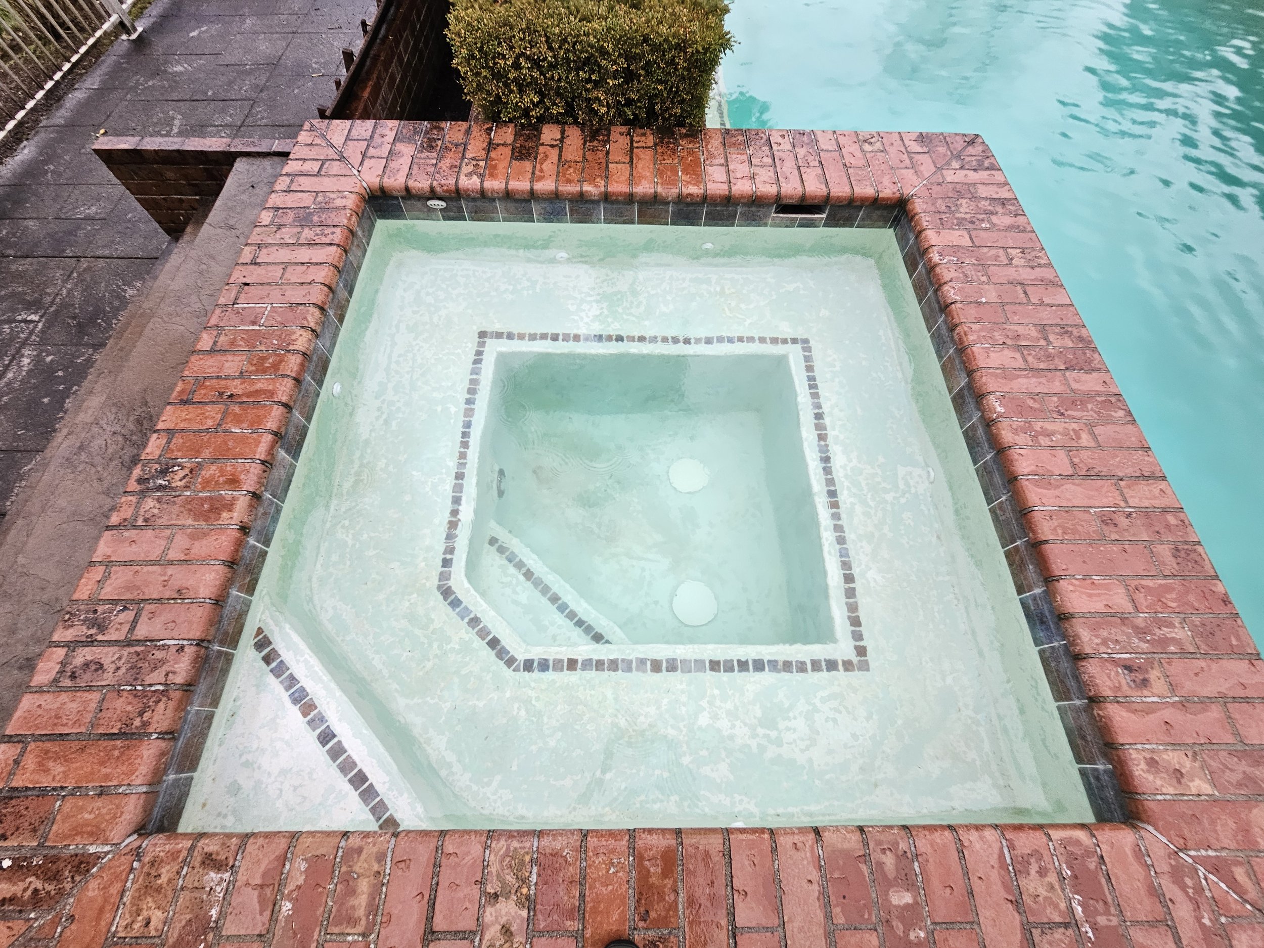 An in ground spa with brick coping and stone tile trim freshly cleaned with clear, light aqua colored water.