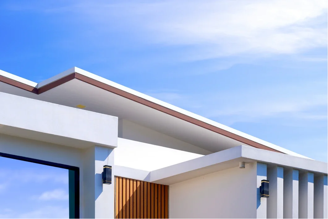 Modern house with white walls and wooden accents, under a blue sky with scattered clouds.