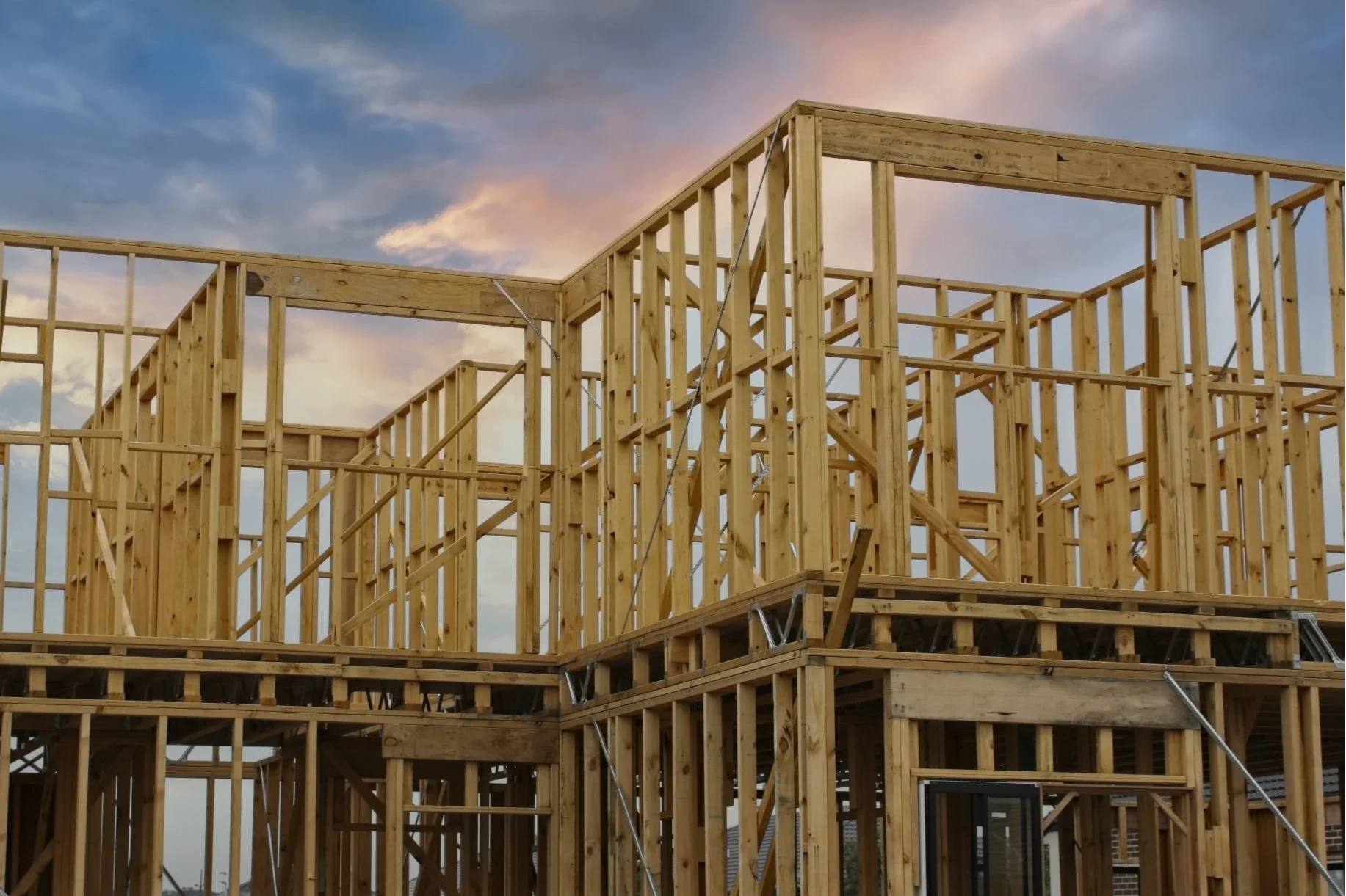 Wooden framing of a house under construction against a sunset sky.