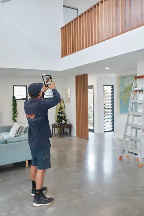 Man taking a photo inside a modern, decorated living room with Christmas decorations, a ladder, and a world map on the wall.