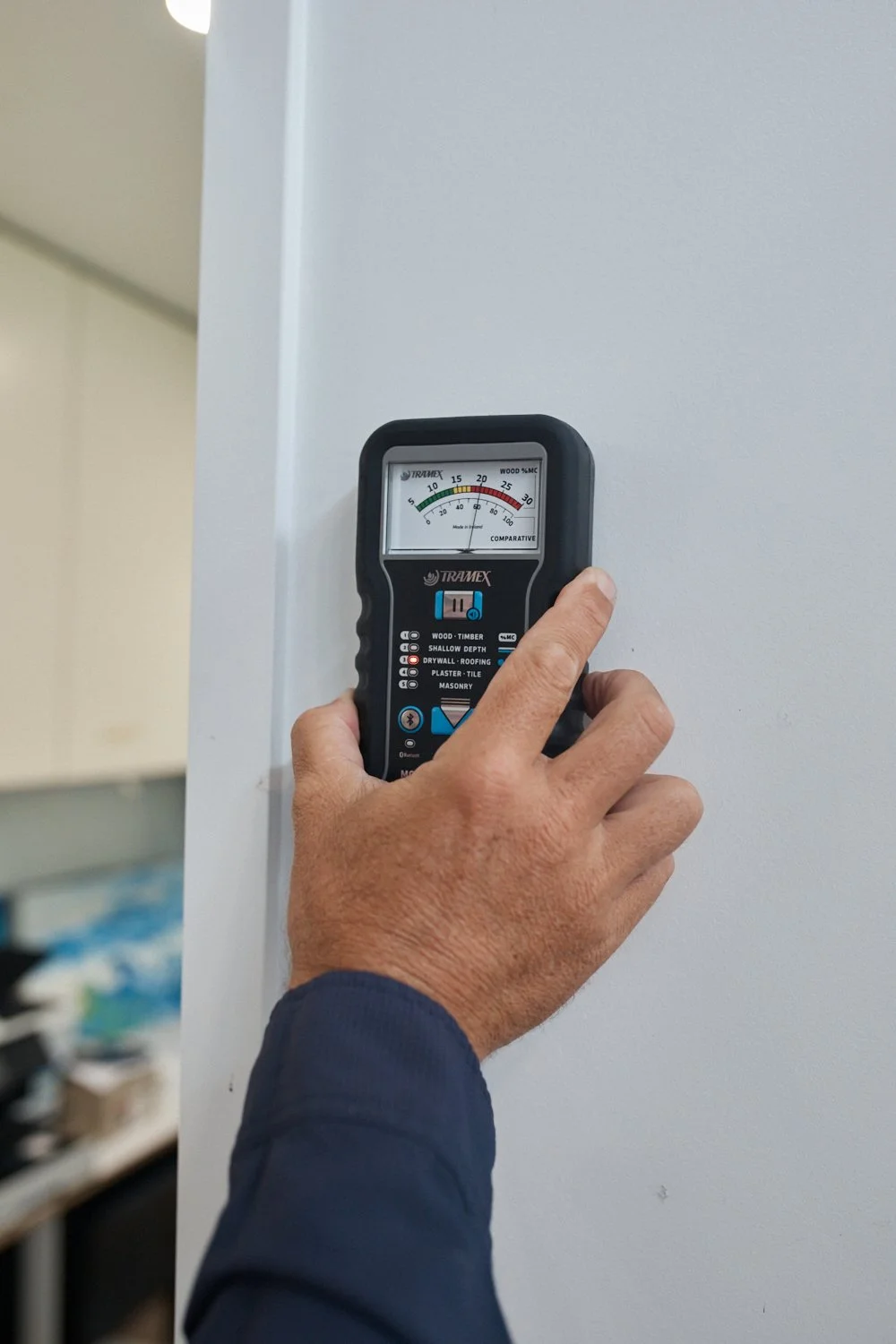 A person using a Tramex moisture meter on a white wall.