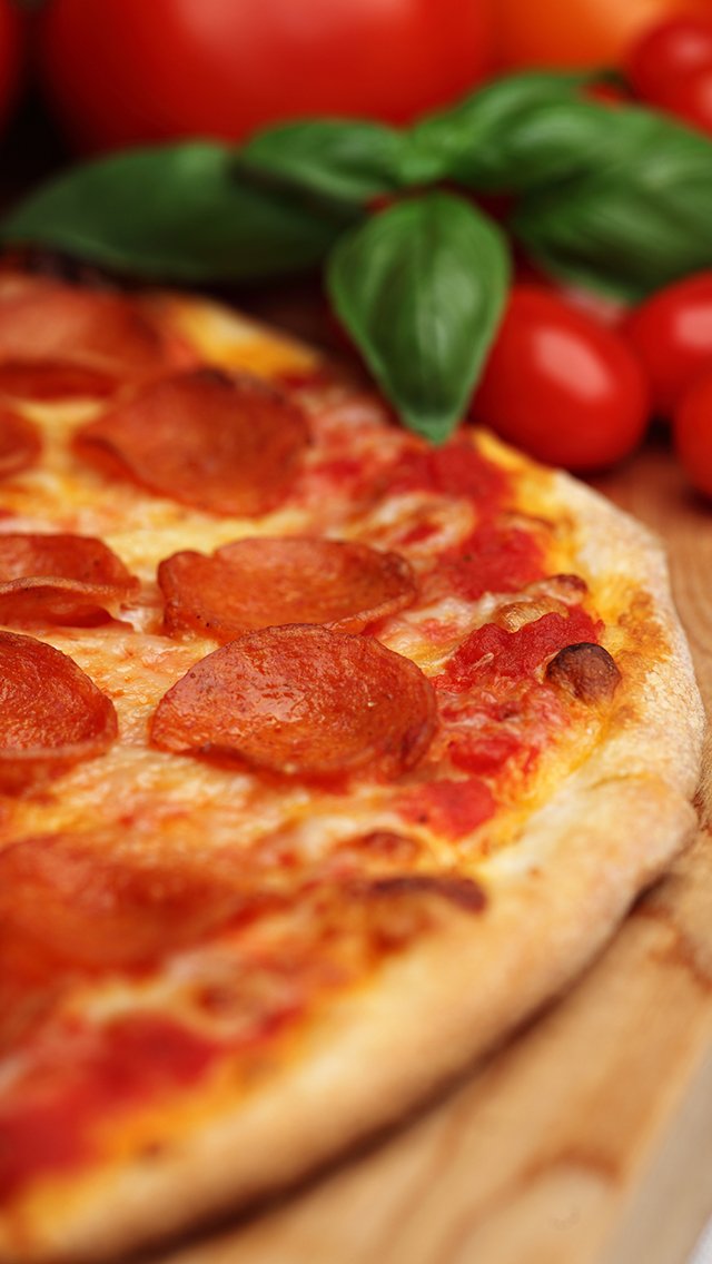Close-up of pepperoni pizza with basil and cherry tomatoes in the background.